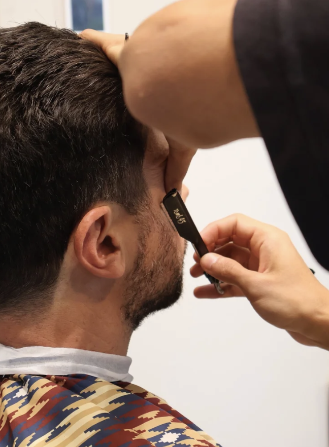 A man getting a haircut, with a barber using clippers on the side of his head.