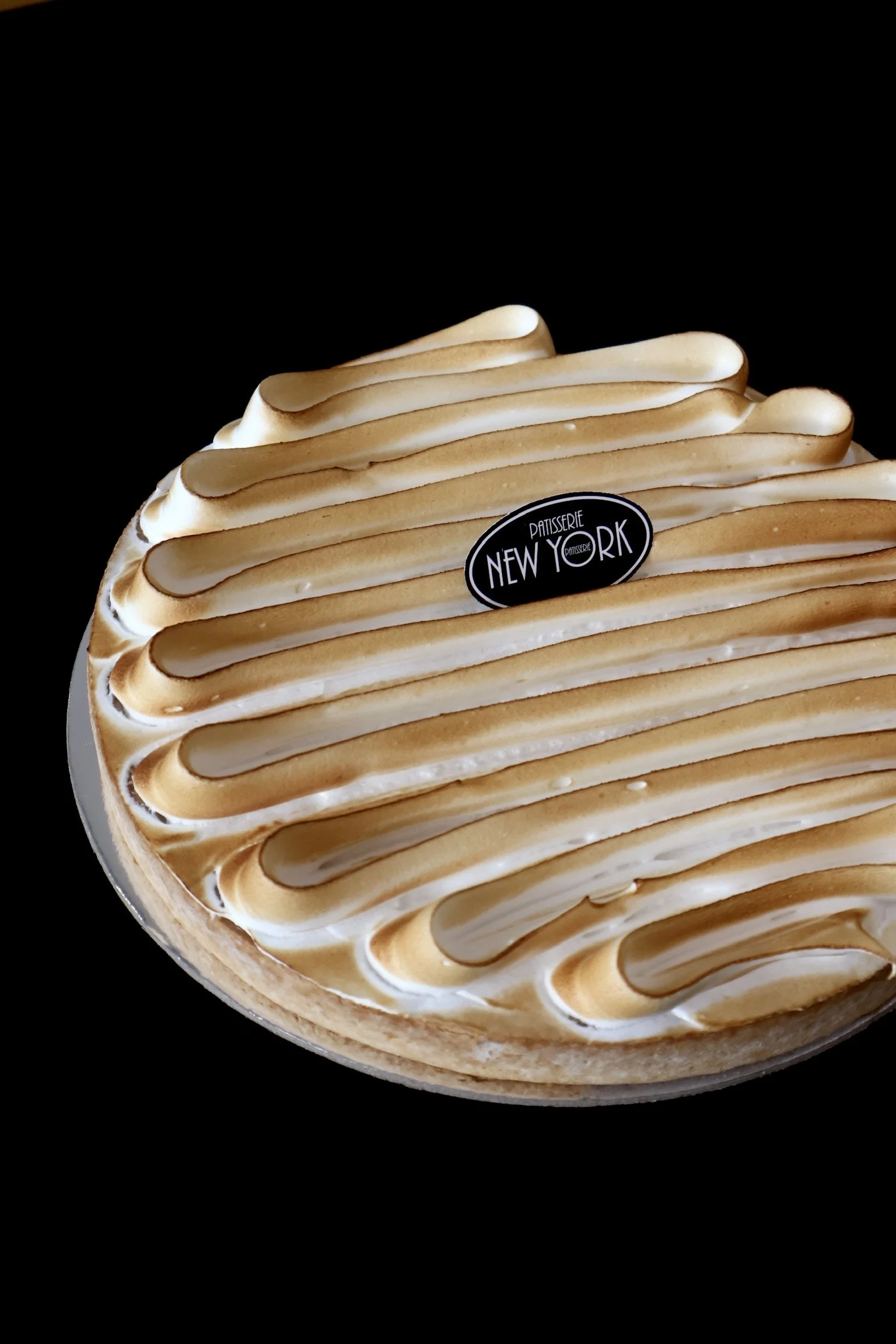 A round lemon meringue tart with toasted meringue topping arranged in peaks on a black background.