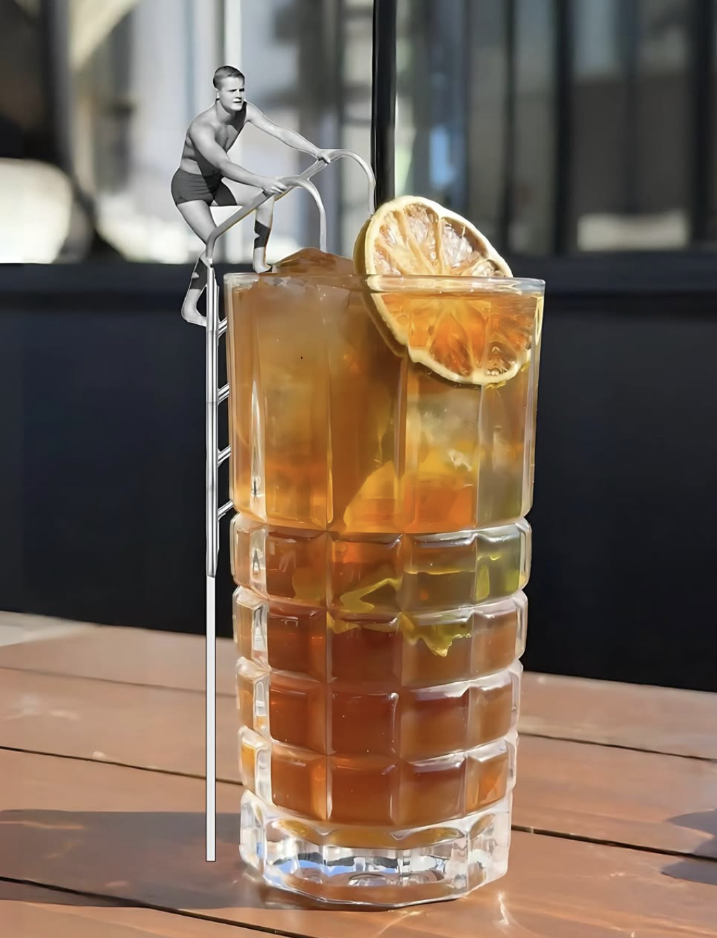 A tall glass of iced tea with a lemon slice garnish on a wooden table, featuring a black and white photo of a woman climbing a ladder, edited into the scene.