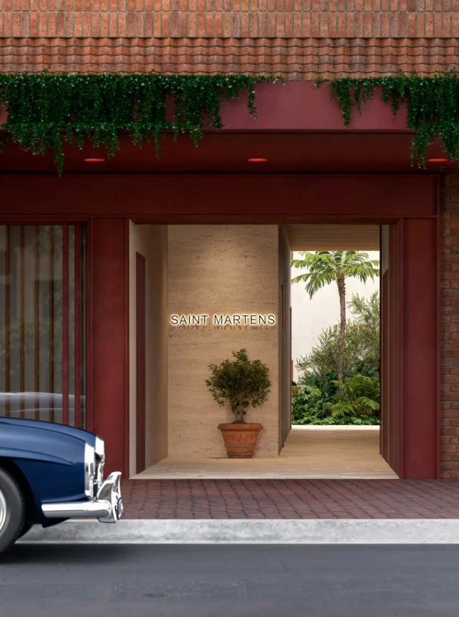Entrance of Saint Martens with a potted plant, tropical trees in the background, and part of a classic blue car visible in the foreground.