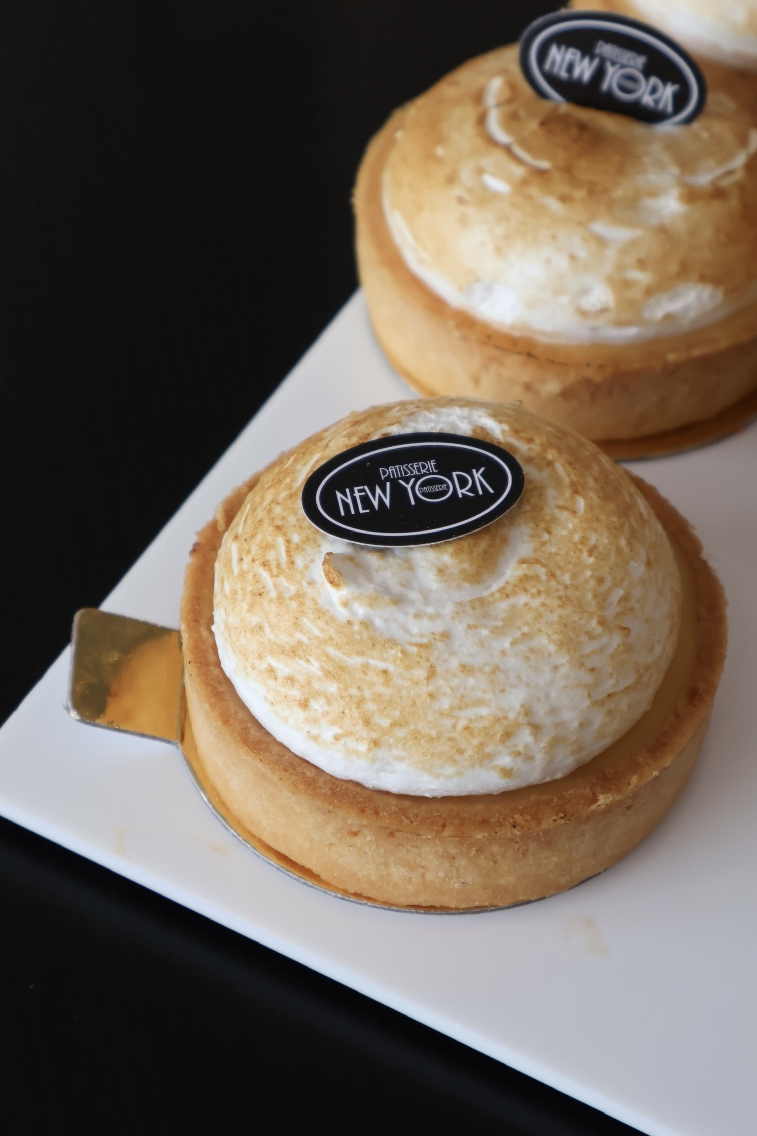 Close-up of two lemon tart pastries with a dollop of whipped cream and a toasted meringue topping, served on a white plate.