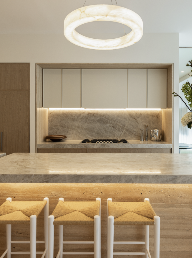Modern kitchen with a marble island, wooden cabinetry, and a built-in stove, illuminated by a circular ceiling light.