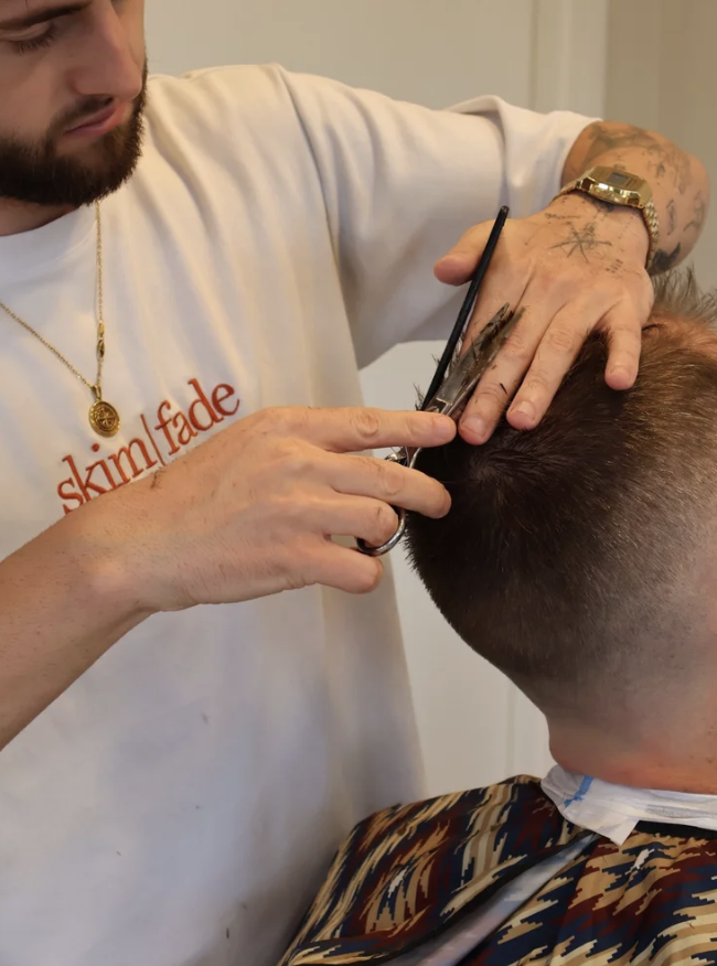 Barber cutting a man's hair with scissors and comb in a barbershop.