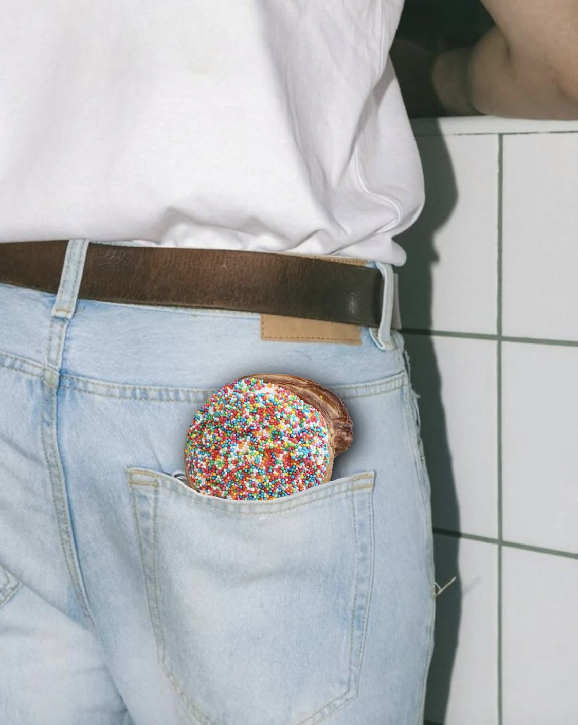A person's back in light blue jeans with a doughnut in their back pocket, decorated with colorful sprinkles.