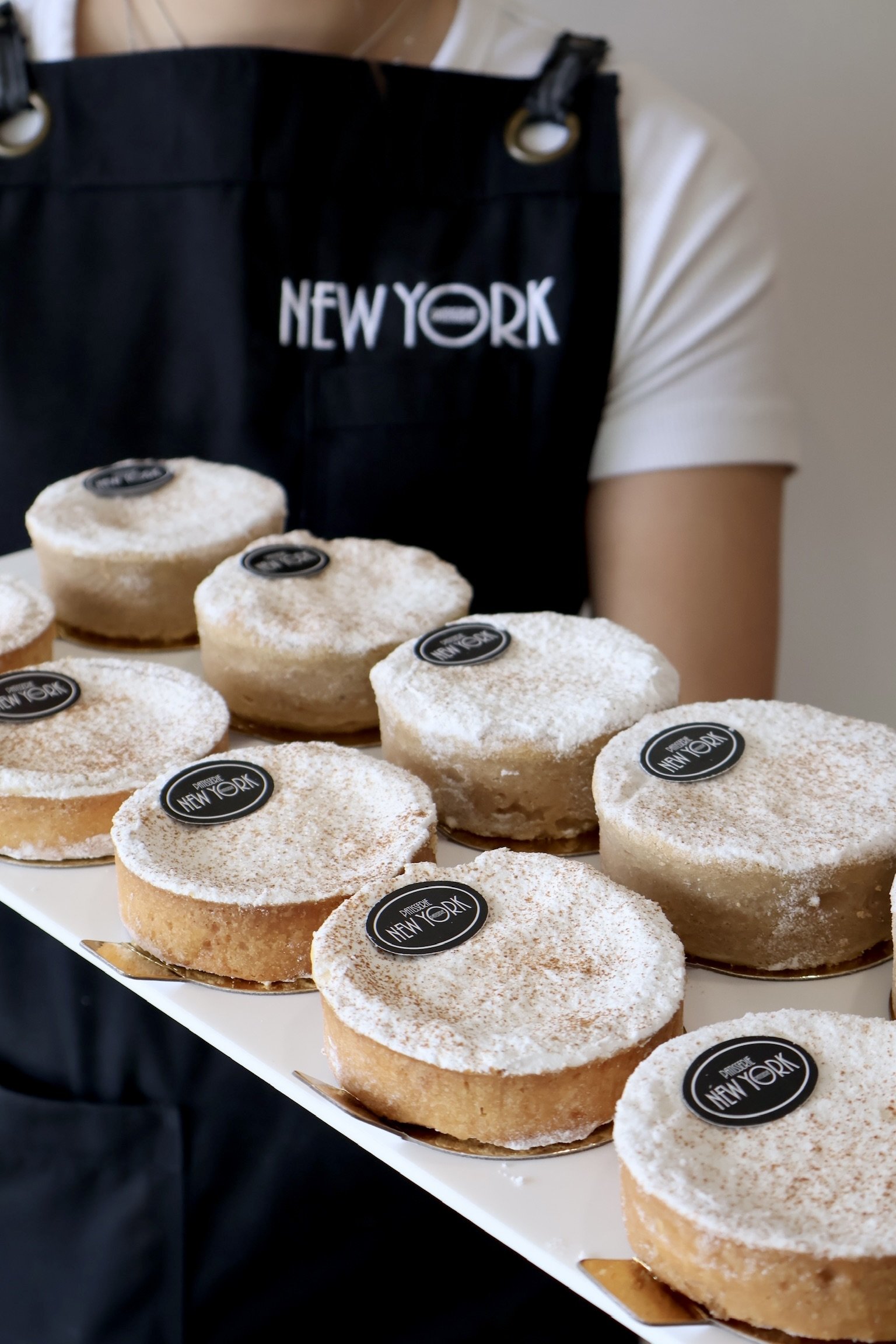 Multiple round donuts with powdered sugar on top, each labeled with 'Mission New York,' on a white tray.