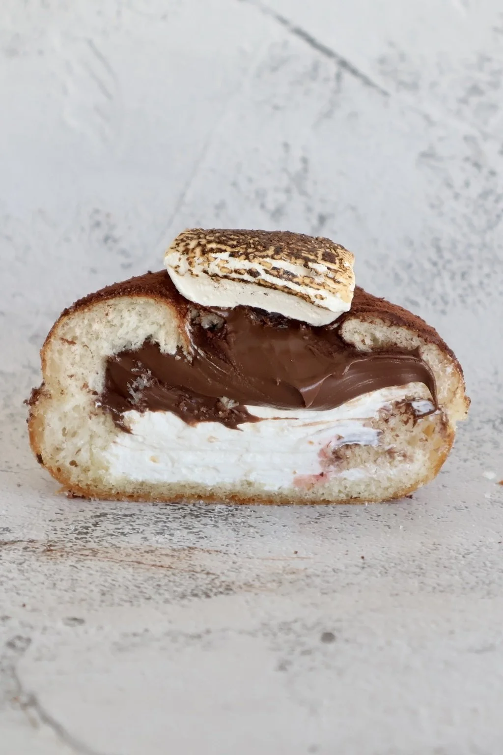 Cross-section of a dessert with cream, chocolate filling, and topped with a toasted marshmallow.