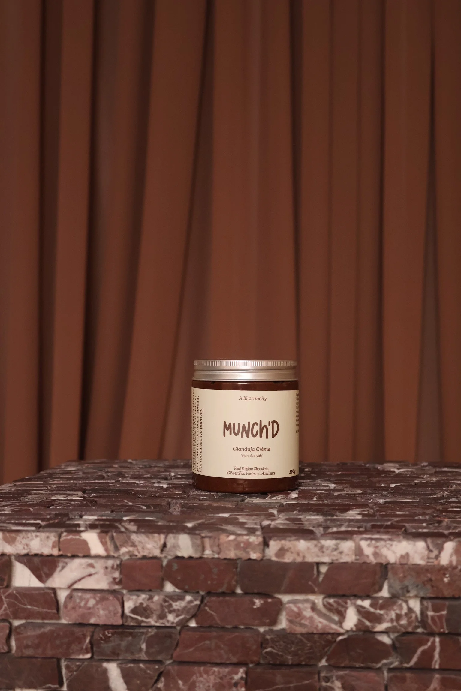 A jar labeled 'MUNCH'D' stands on a brick surface with a wooden wall background.