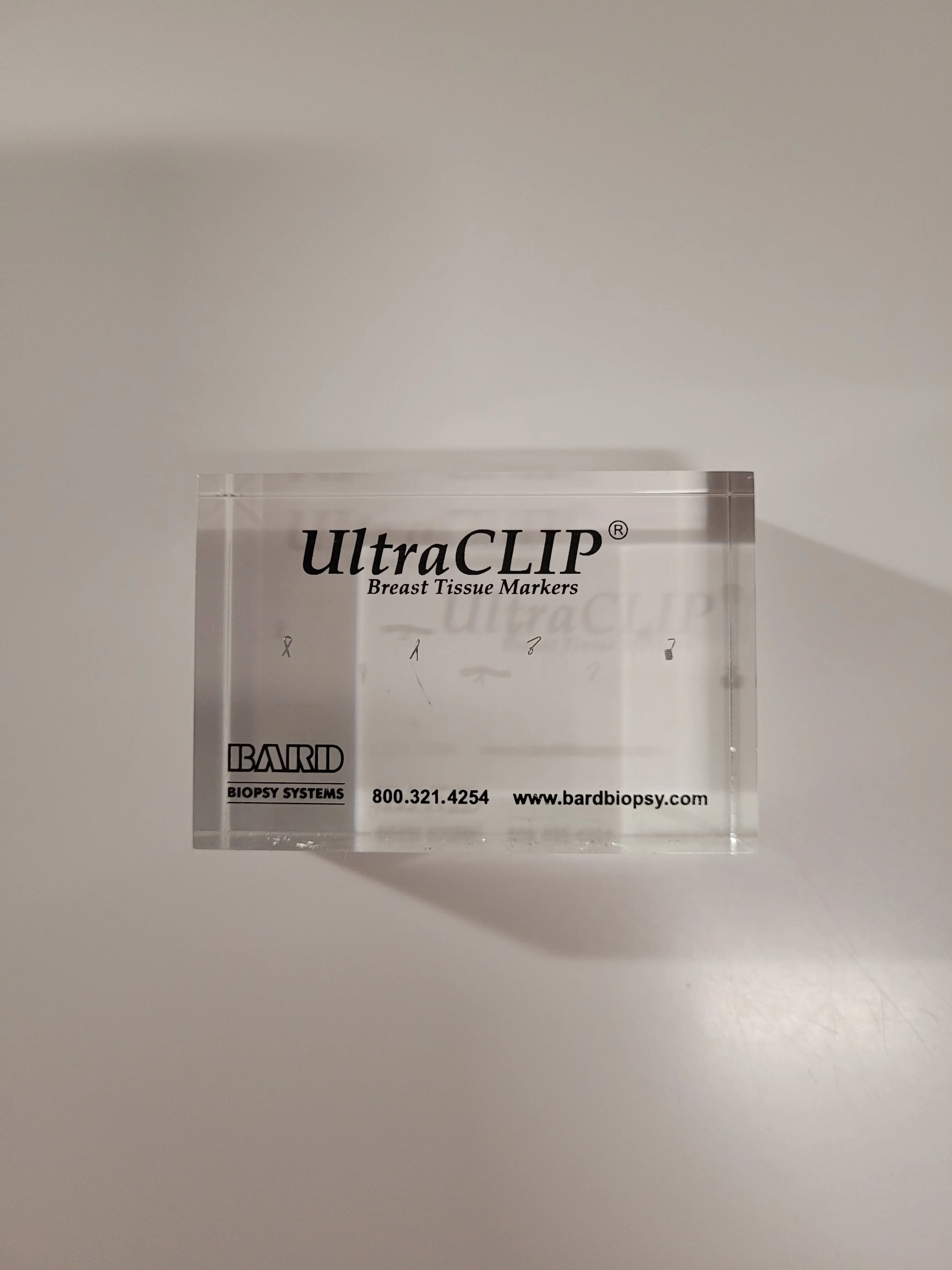 A clear acrylic block with the label 'UltraCLIP Breast Tissue Markers' and company information from Bard Biopsy Systems.