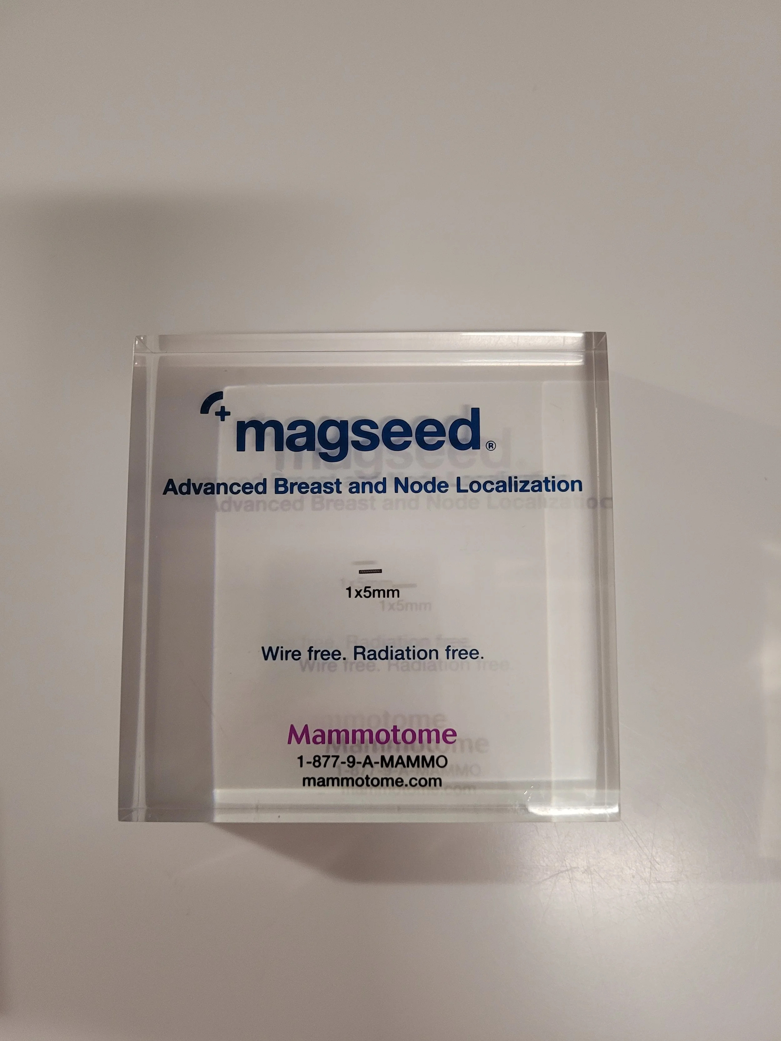 A transparent sign with blue and purple text displaying 'maged' logo, 'Advanced Breast and Node Localization', a scale, and the words 'Wire free. Radiation free.' with contact information for Mammotome.