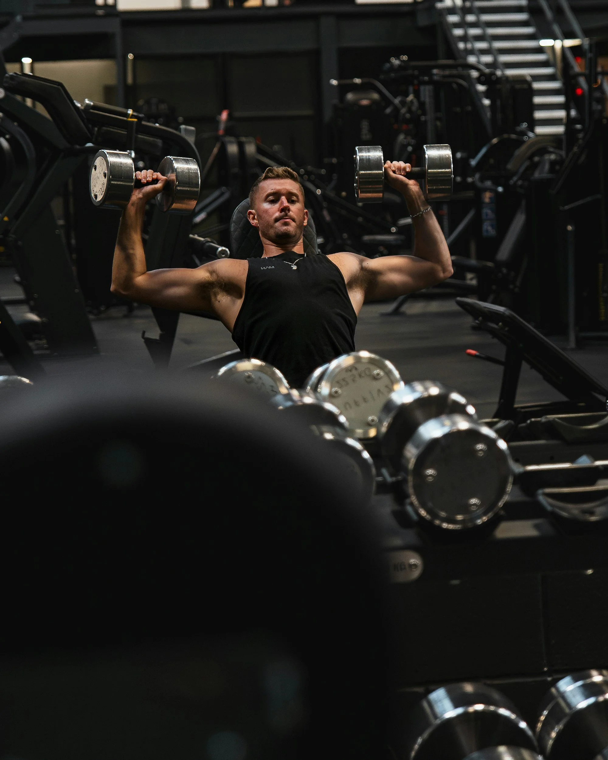 A man lifting dumbbells in a gym, surrounded by various exercise equipment.