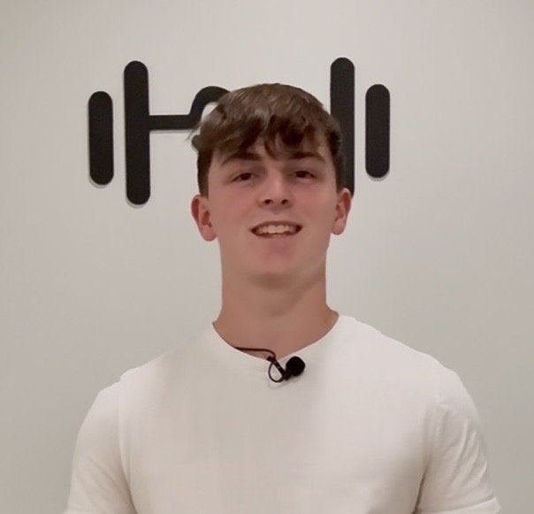 A man with curly dark hair, glasses, and a beard looking to the right with a slight smile.