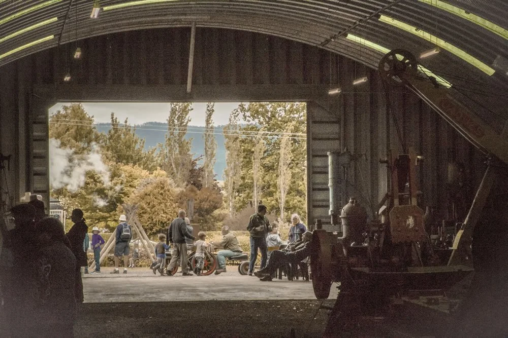 View from inside Pearn's Steam World, looking out at a group of people, including children, gathered outdoors near trees and a mountain landscape.