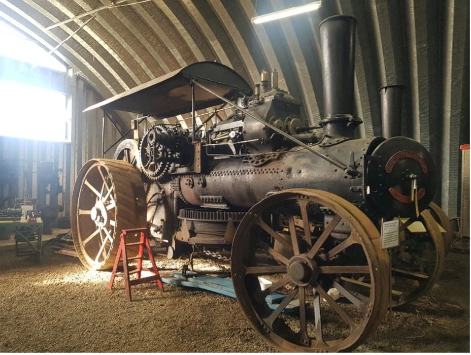 A vintage steam-powered tractor with large metal wheels displayed in a museum.
