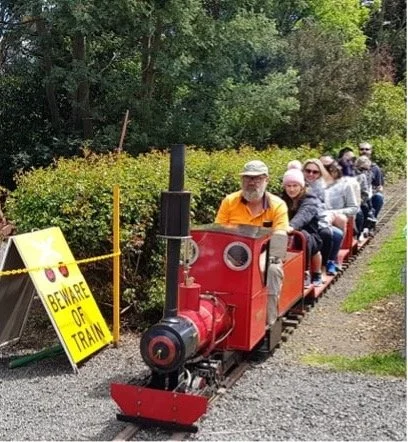 People riding a small red train on a track in a park