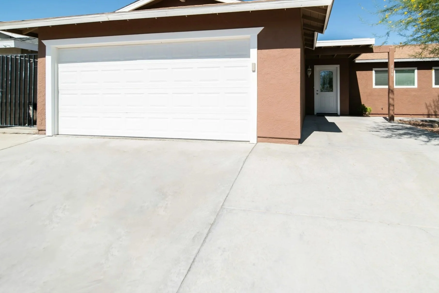 A single-story house with a light brown exterior, white garage door, front door, small window, and driveway.
