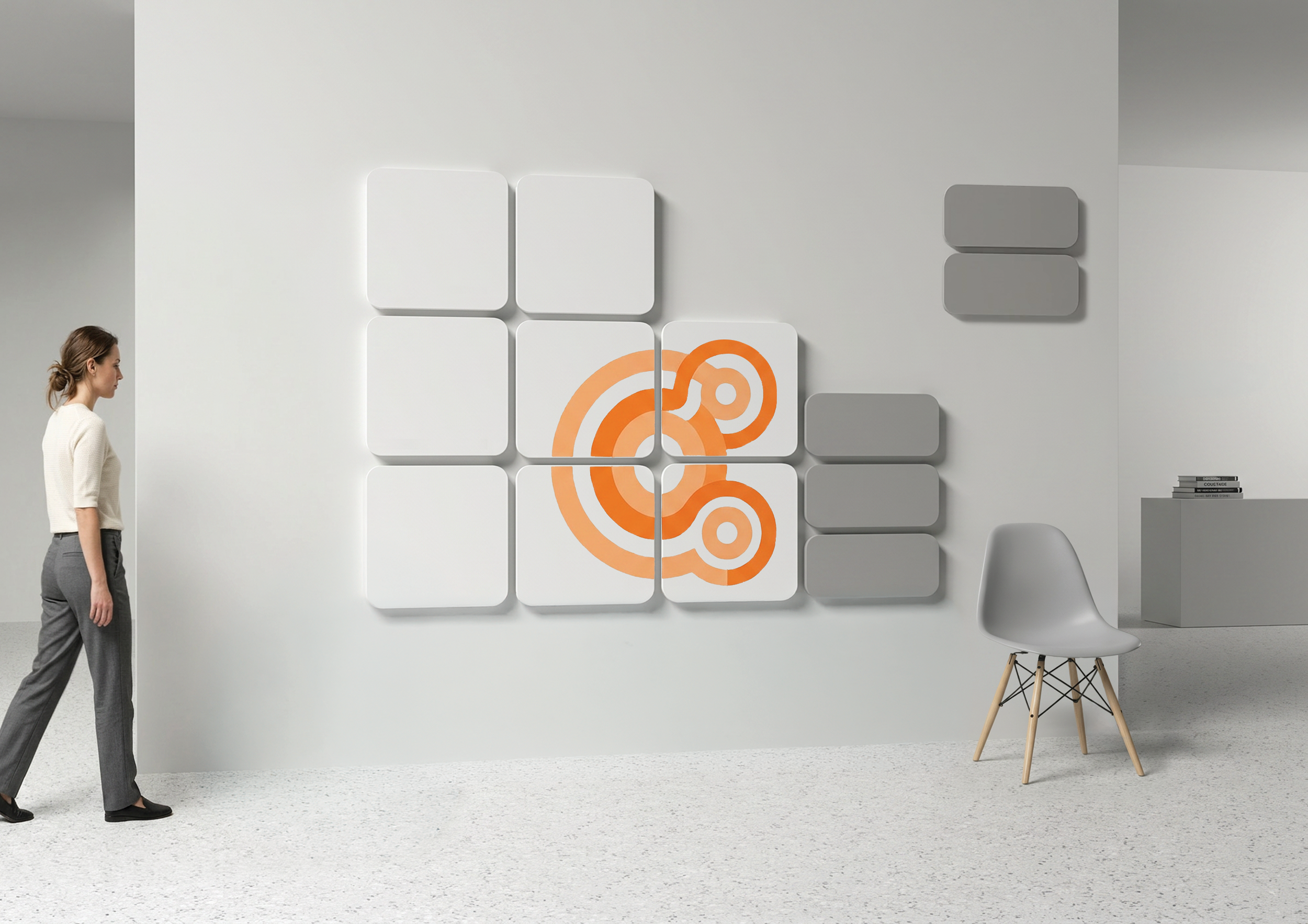 A woman in gray pants and a white top walking in a minimalist modern interior with a white wall decorated with abstract orange circular art and square gray panels. There is a white chair with wooden legs and a small stack of books on a side table.