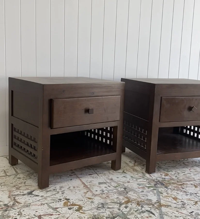 Two dark brown wooden nightstands with a drawer and open shelf, positioned on a paint-splattered floor against a white paneled wall.
