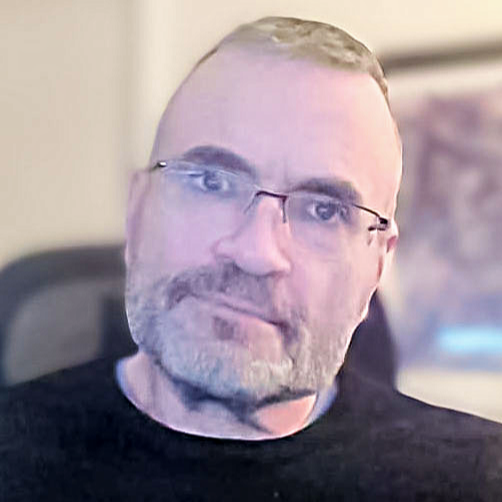 A man with hair and glasses smiling compassionately