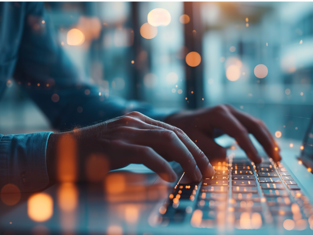 Close-up of hands typing on a laptop keyboard with a blurred cityscape and bokeh lights in the background.