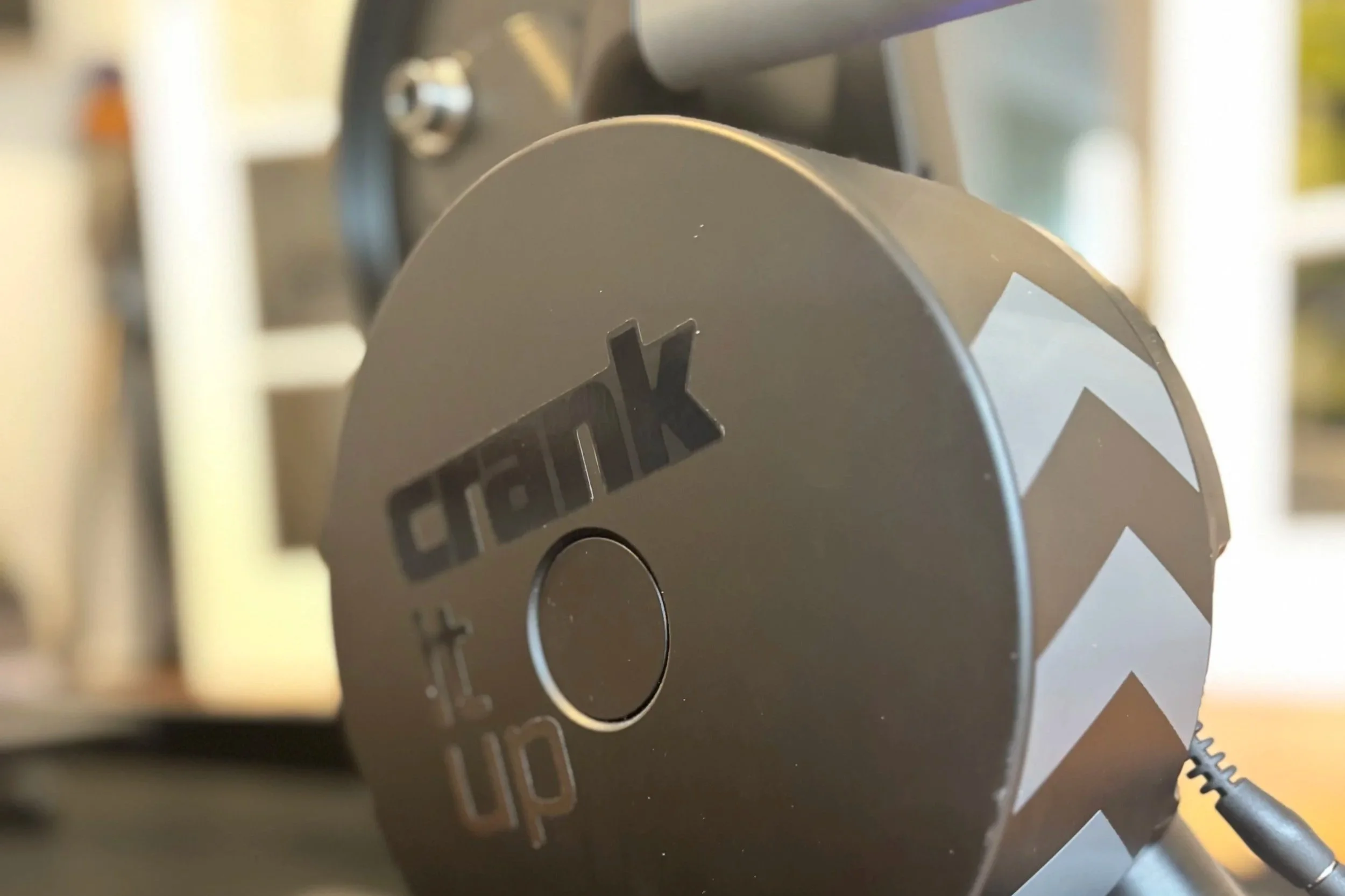 Close-up view of a metallic mechanical part, featuring engraved text and circular shapes, with some visible screws and a power cord on the right side.