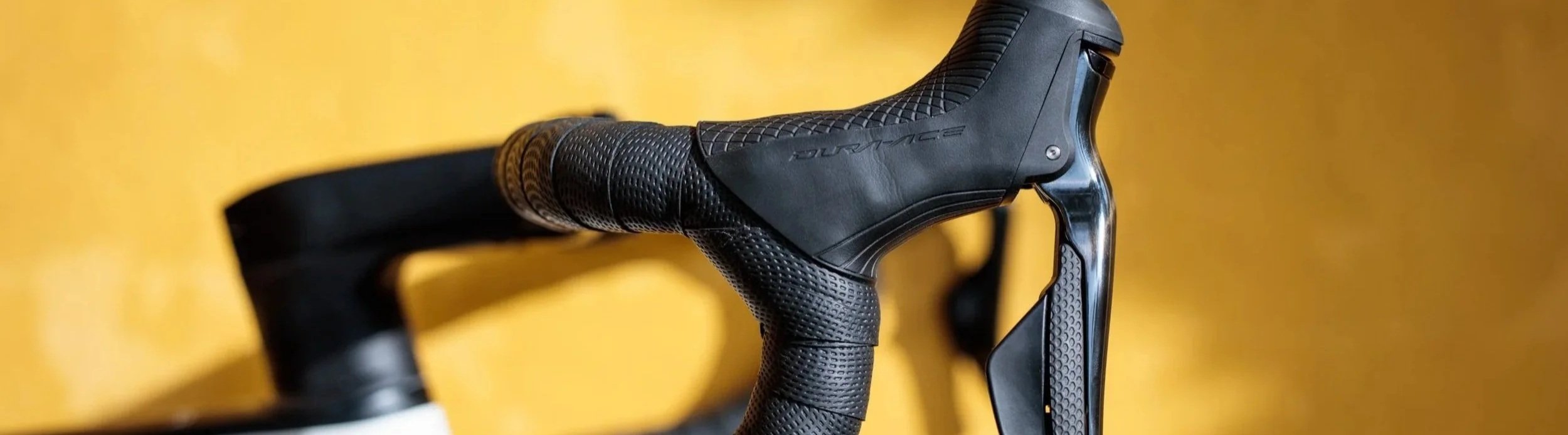 Close-up of a black bicycle handlebar and gear shifter against a yellow background.