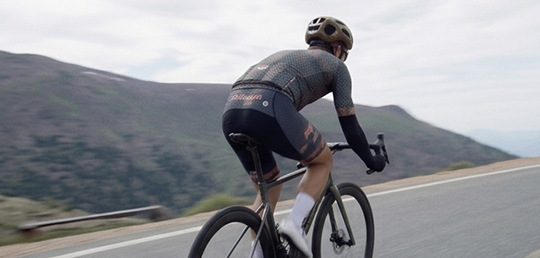 A cyclist riding a bike on a mountain road with mountains in the background.