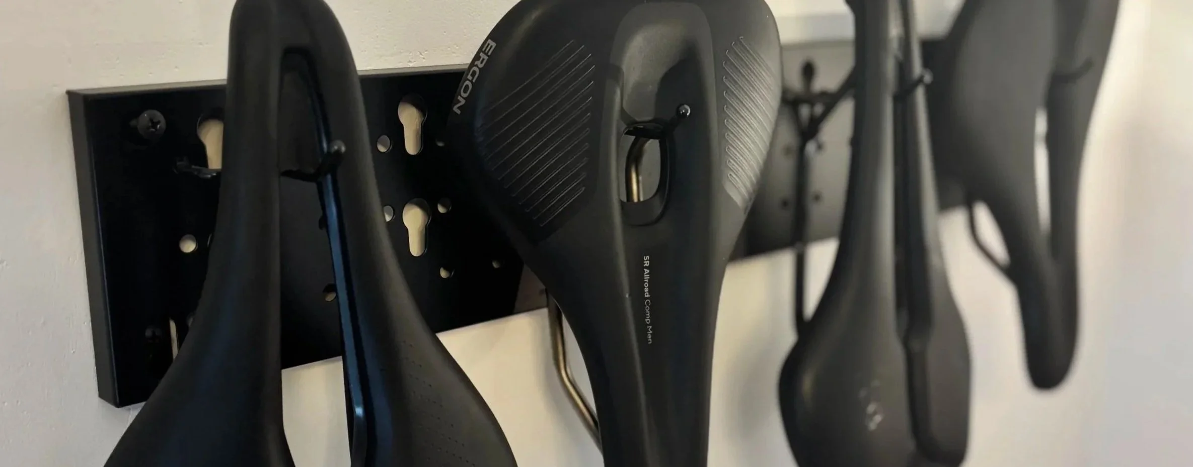 Close-up of a wall-mounted storage rack holding multiple black bicycle saddles.