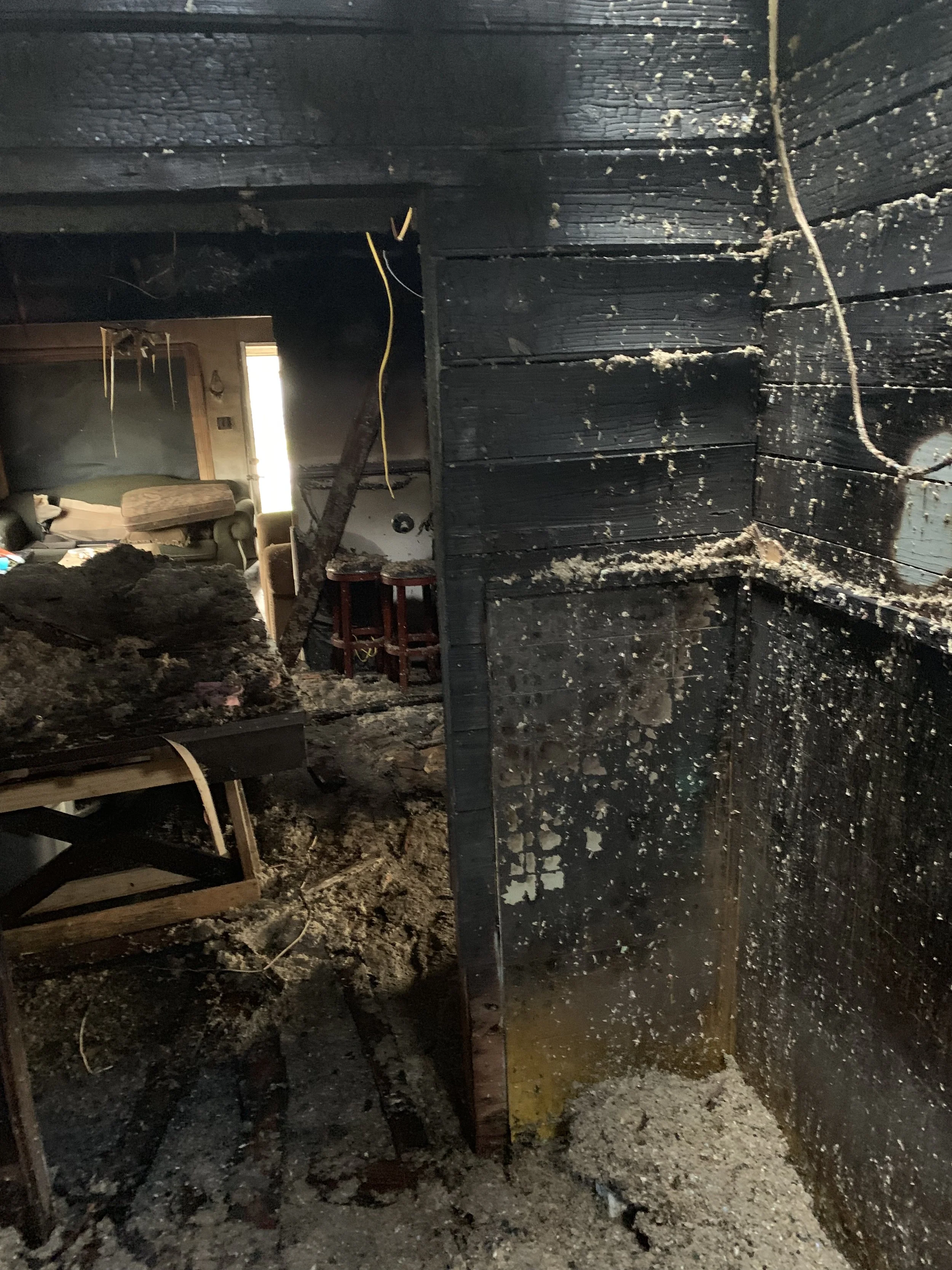 A burned interior room with blackened walls, debris on the floor, and visible water damage.