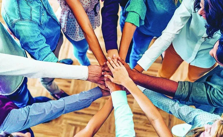 Group of diverse people placing hands together in a circle, symbolizing unity and teamwork.