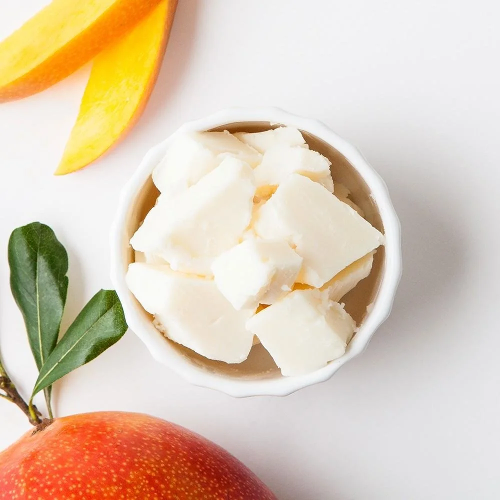 A bowl of white chocolate chunks, with slices of mango and an apple on a white background.