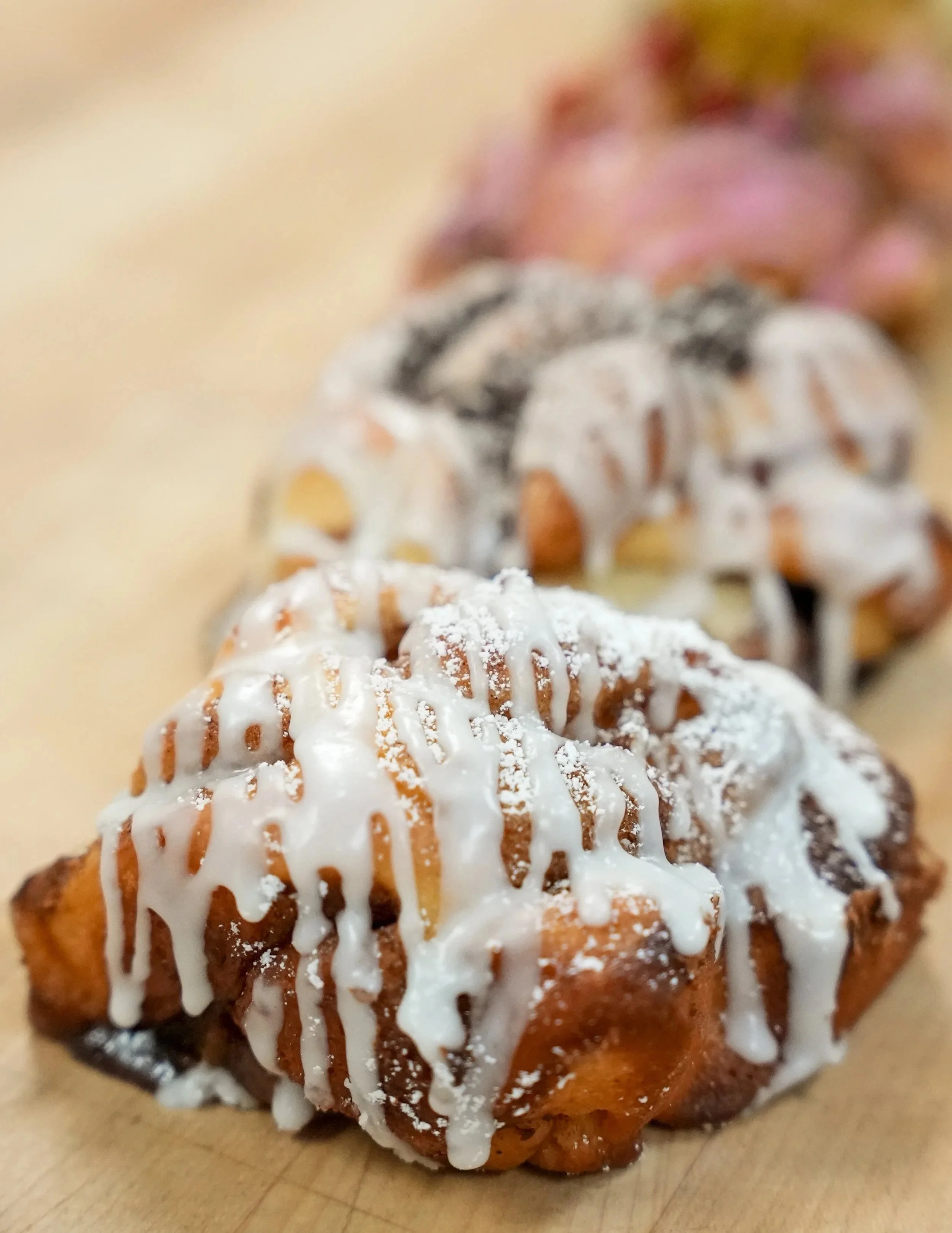 Close-up of three cinnamon rolls topped with white icing and powdered sugar, on a wooden surface.