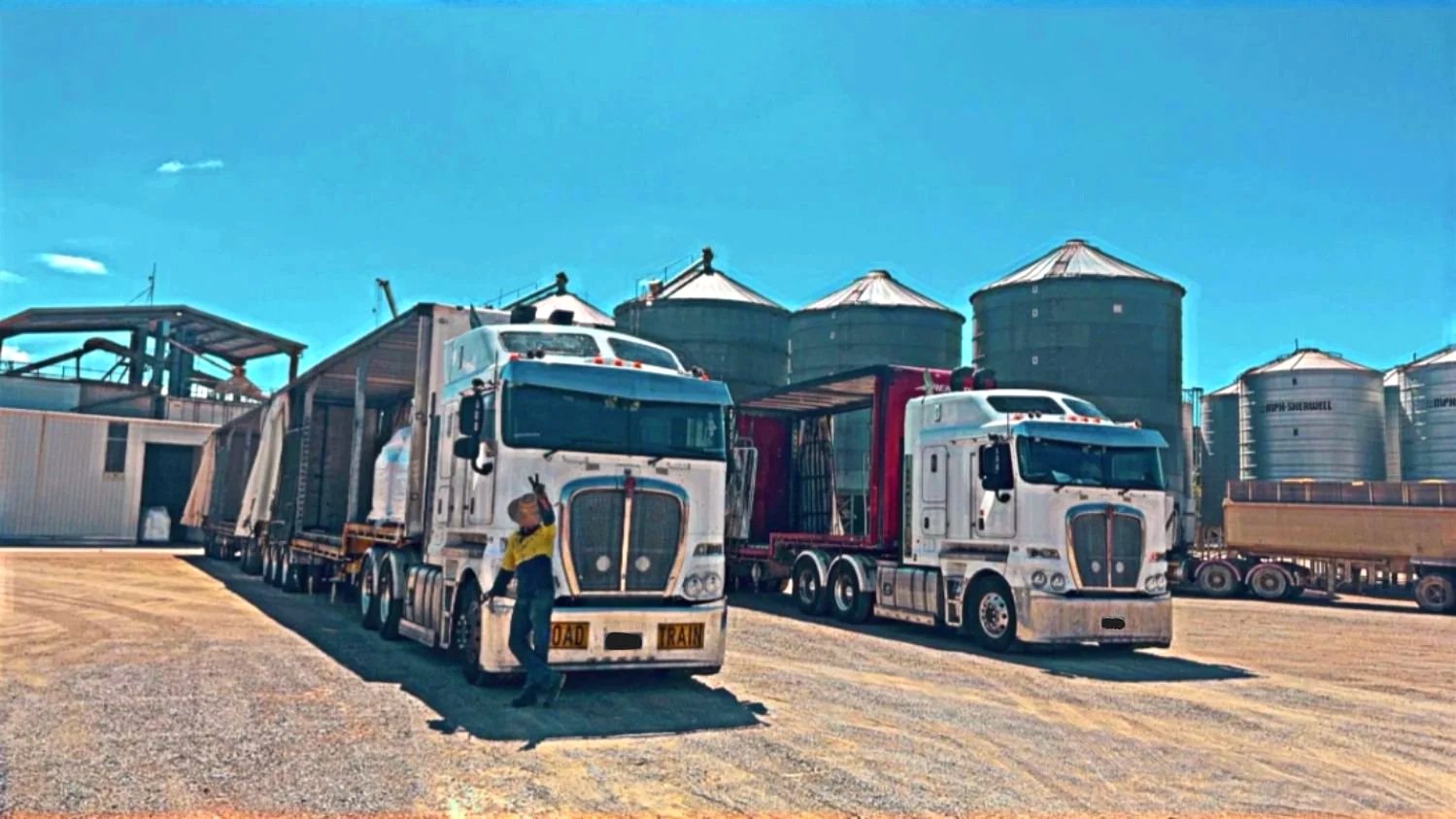 Road train and prime mover and tautliner with Agriculture grain silos or mining silos in the background.