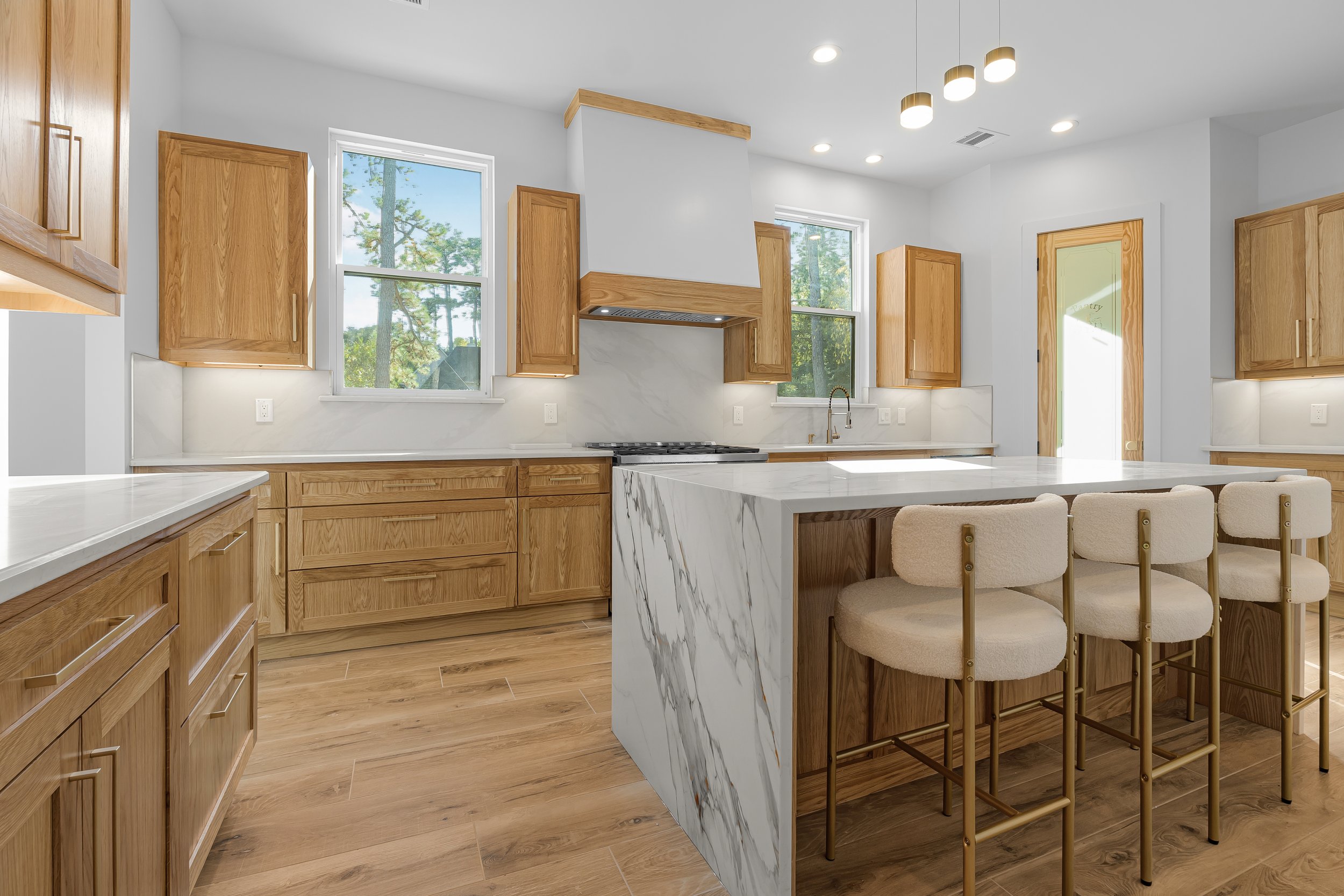 Modern kitchen with wooden cabinetry, white countertops, and a large marble island with four beige chairs.