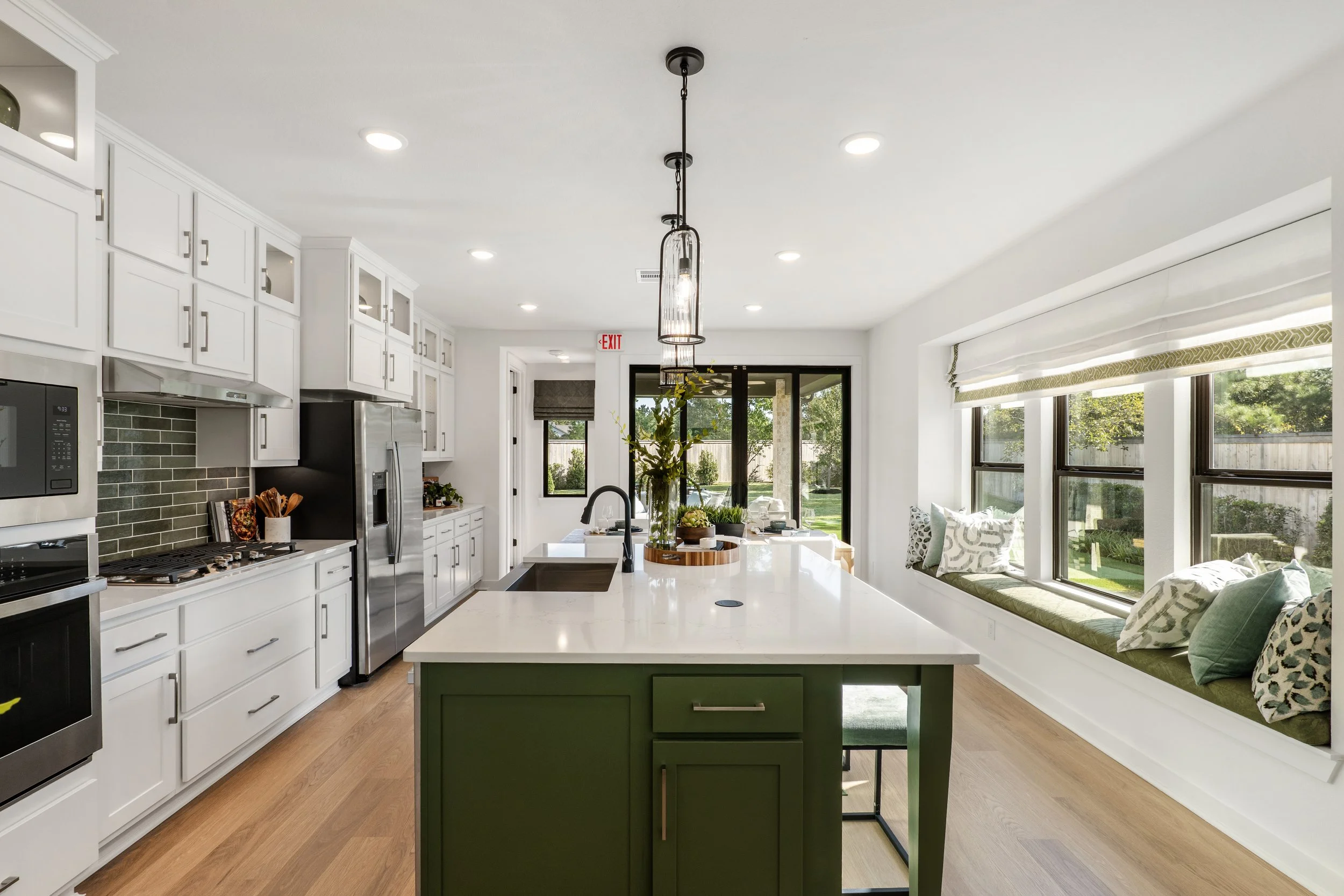 Bright kitchen with white cabinets, a green kitchen island, stainless steel appliances, a window seat with pillows, and a sliding glass door leading to the backyard.