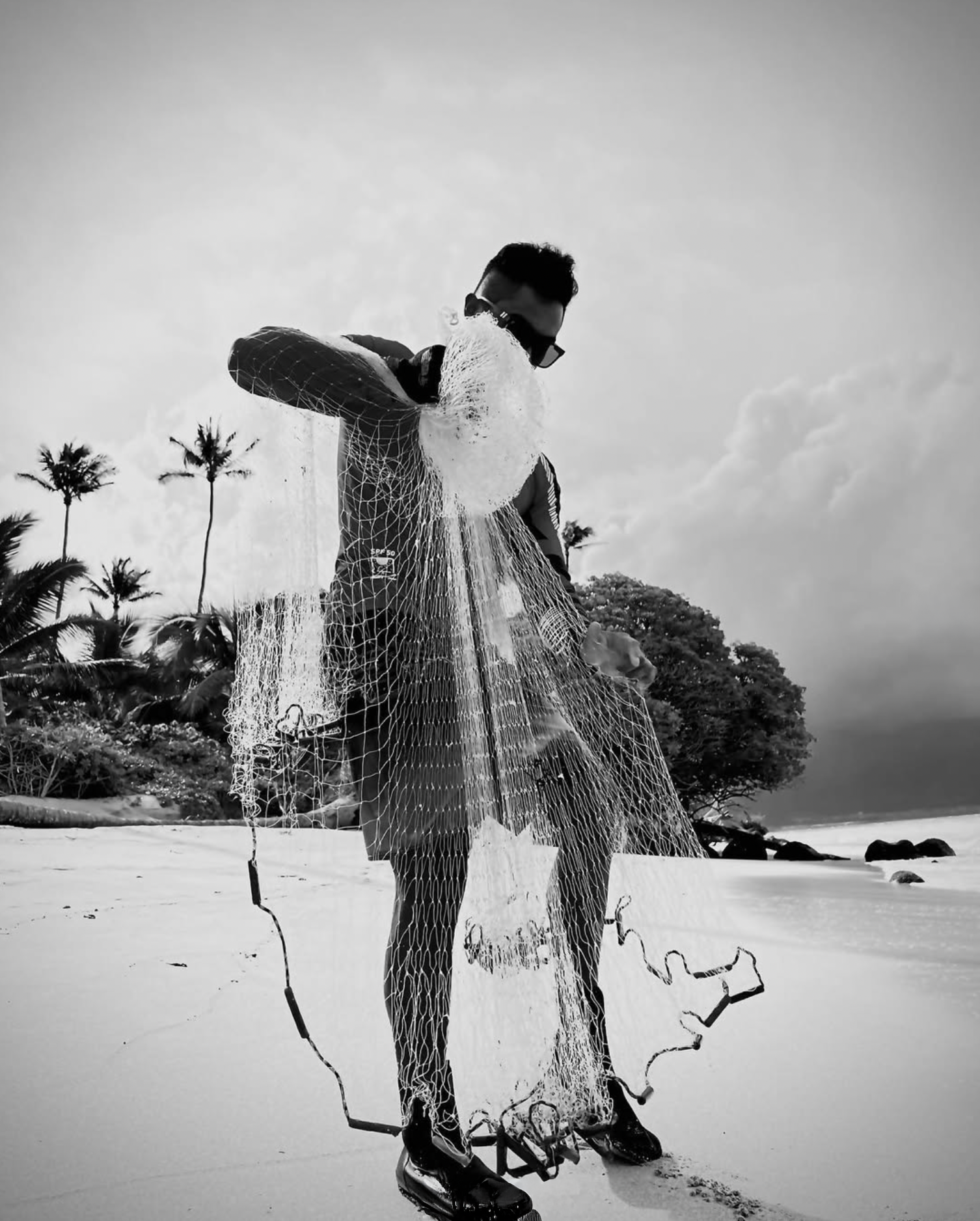 Jason Bero wearing sunglasses standing on a beach holding a fishing net.