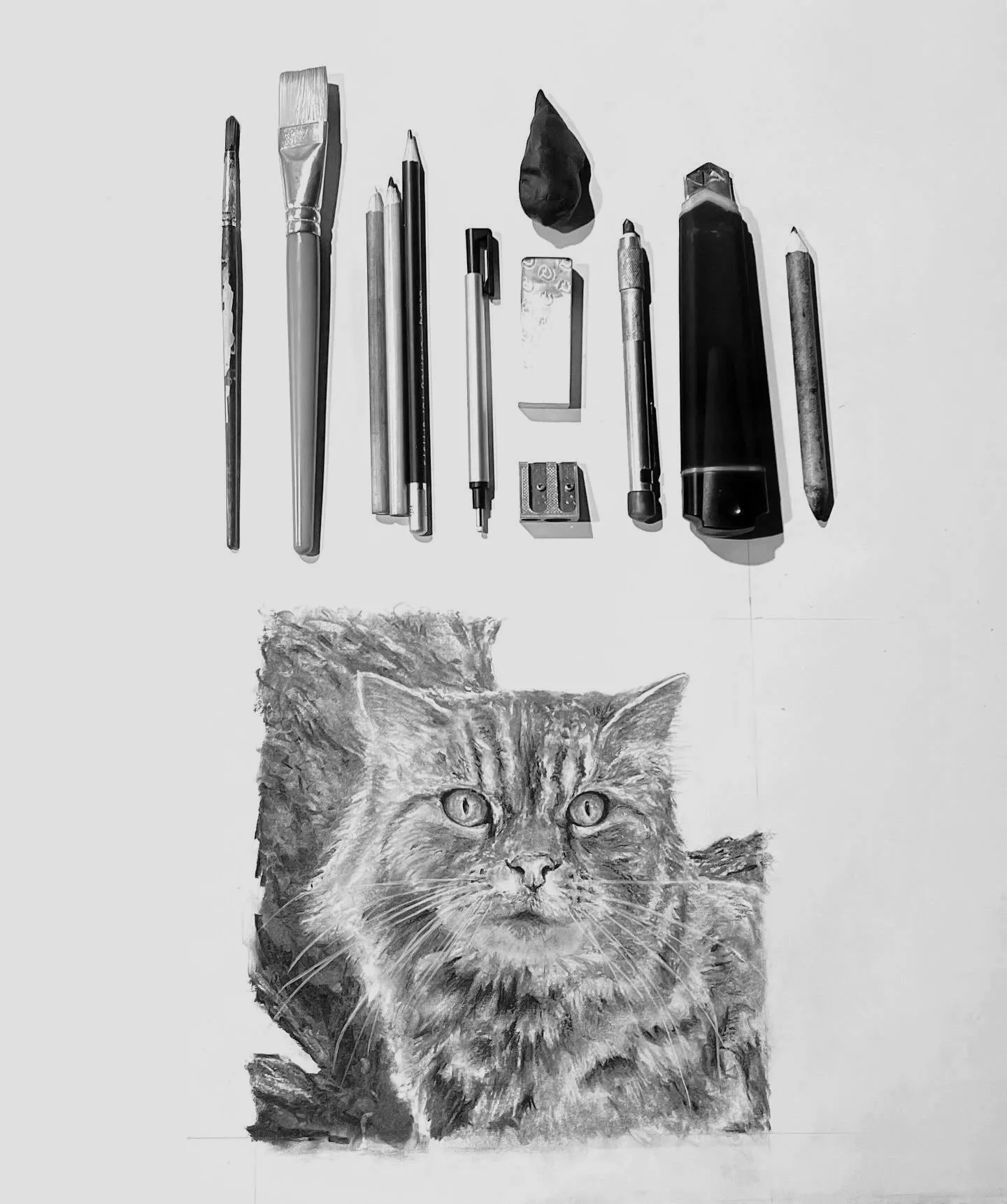 A charcoal drawing of a cat's face with detailed fur and expressive eyes, placed below a collection of various drawing tools on a white background by artists Jason Bero.