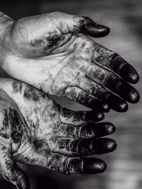 Close-up of dirty, painted, or ink-stained hands with fingers slightly curled against a blurred background.