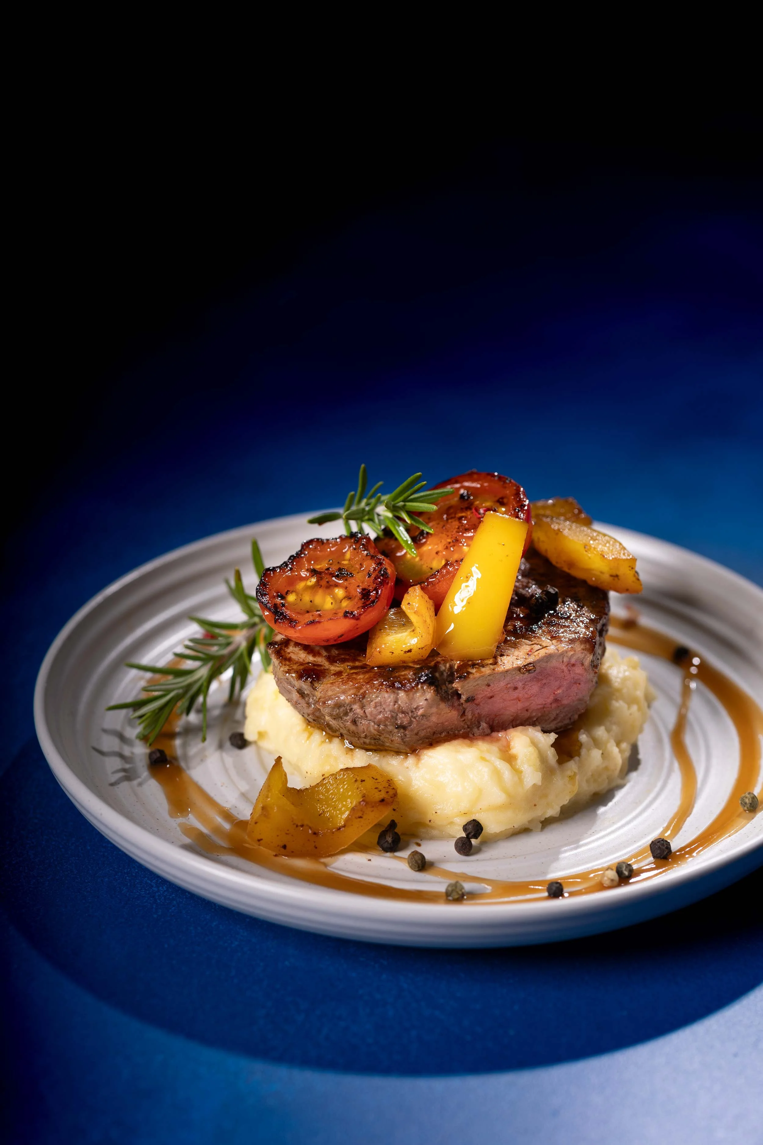A beautifully seared rare steak, tender and pink at the centre, sits atop a bed of creamy mashed potato. It’s finished with sweet grilled capsicum and juicy tomato, lightly charred to bring out their natural richness, for a bold yet comforting plate 