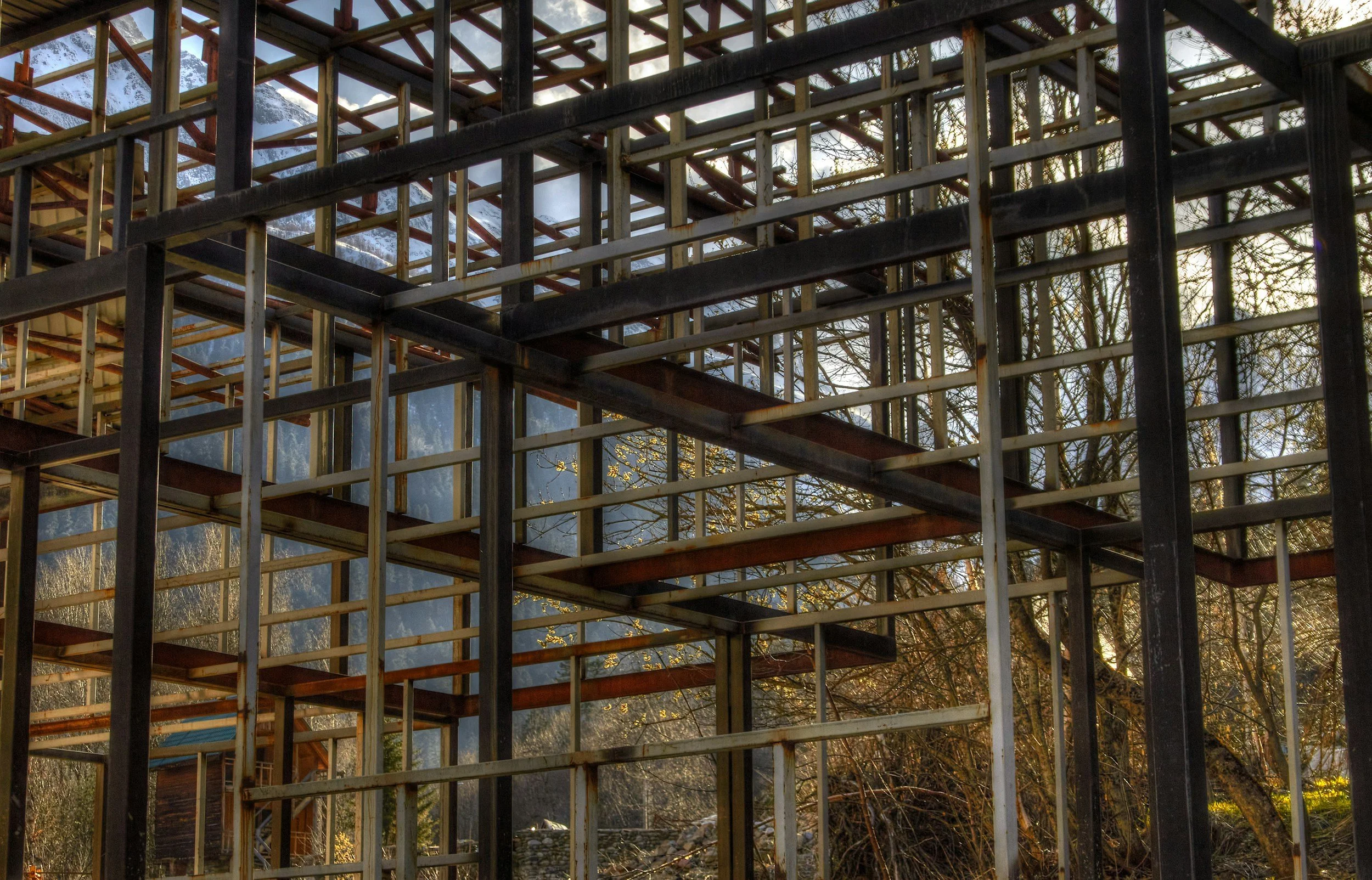 The image shows a construction framework made of metal and wood beams, with some sections still under construction, set outdoors with trees and a mountain in the background.