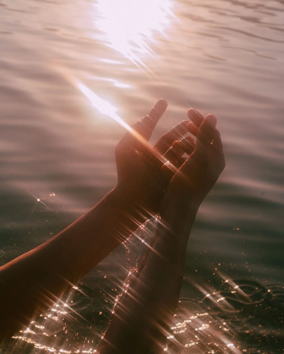 A hand reaching out of water with ripples, capturing sunlight that creates a sparkling effect on the water surface