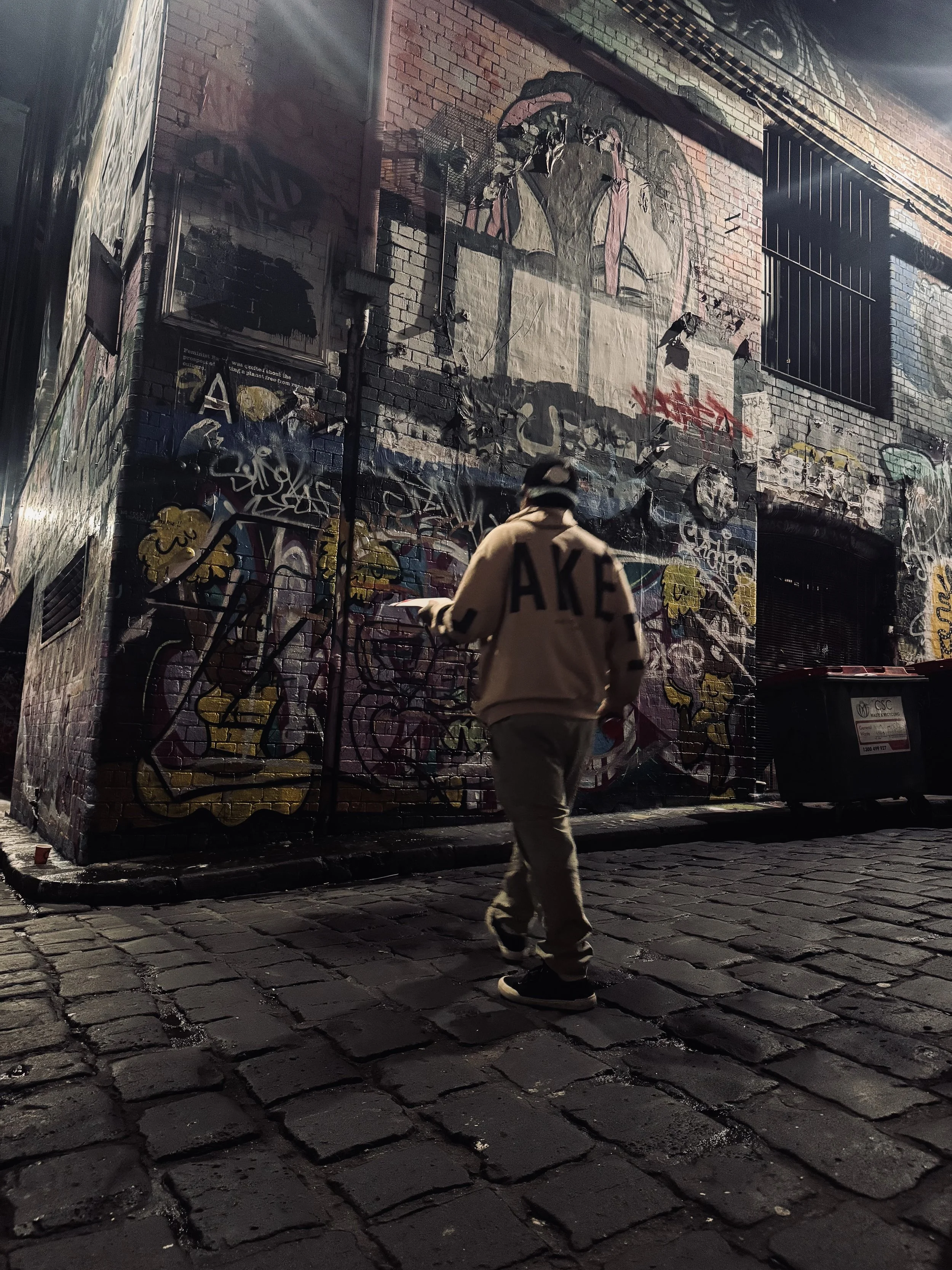 A person walking on a cobblestone street at night, in front of a wall covered in graffiti art.