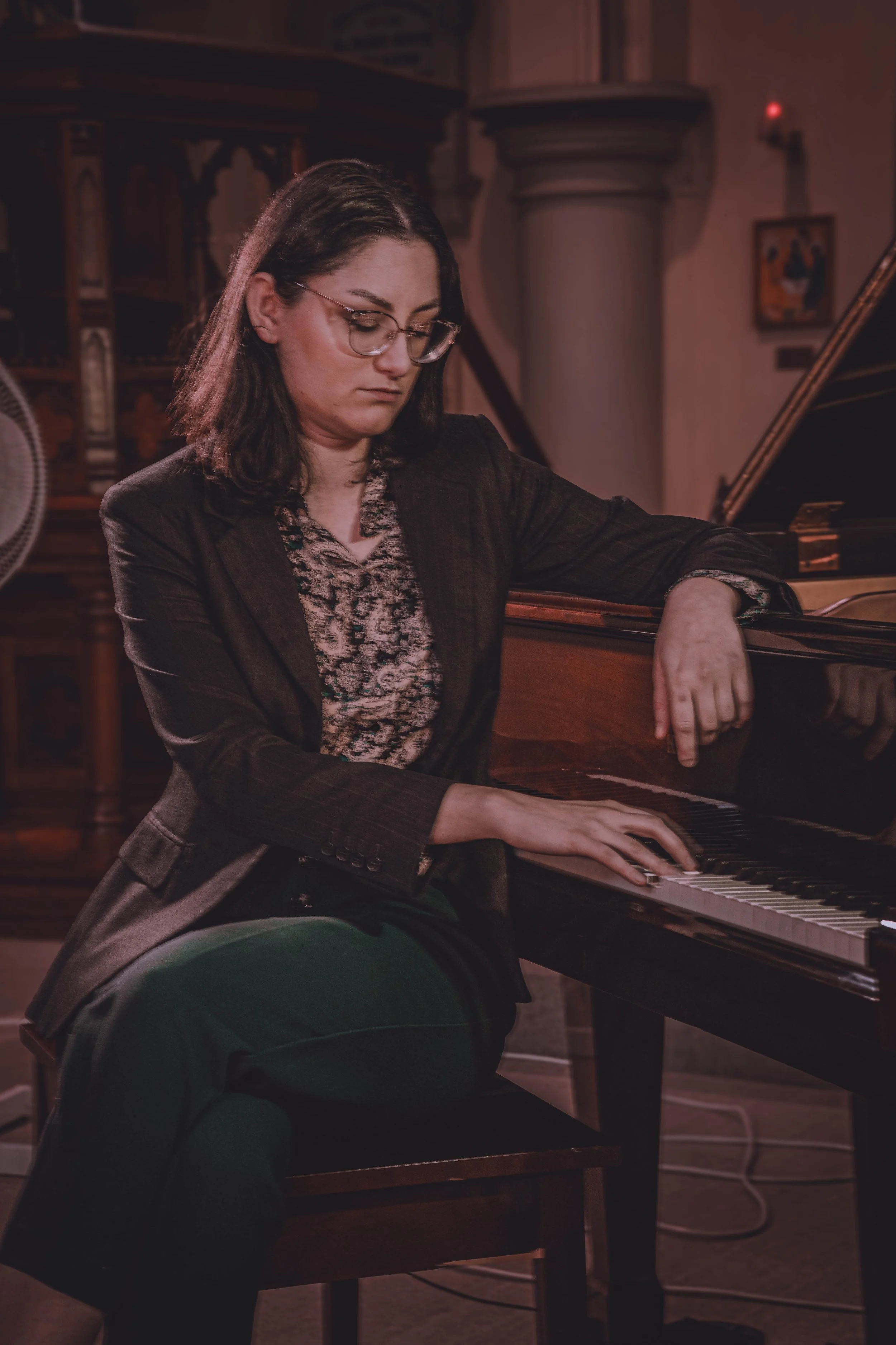 Woman with glasses and dark hair playing piano in a dimly lit room