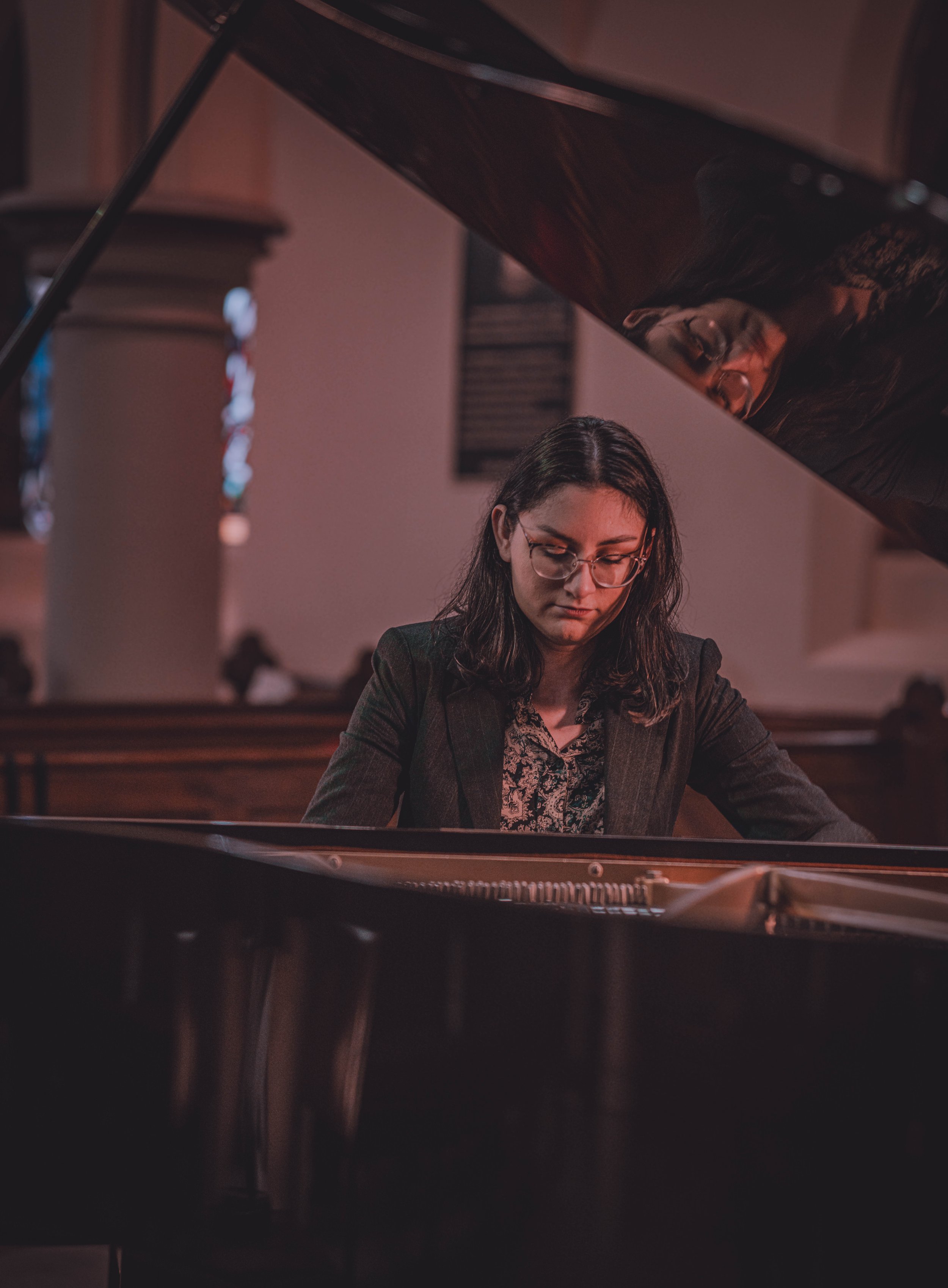 A woman with glasses playing a grand piano in a concert hall.