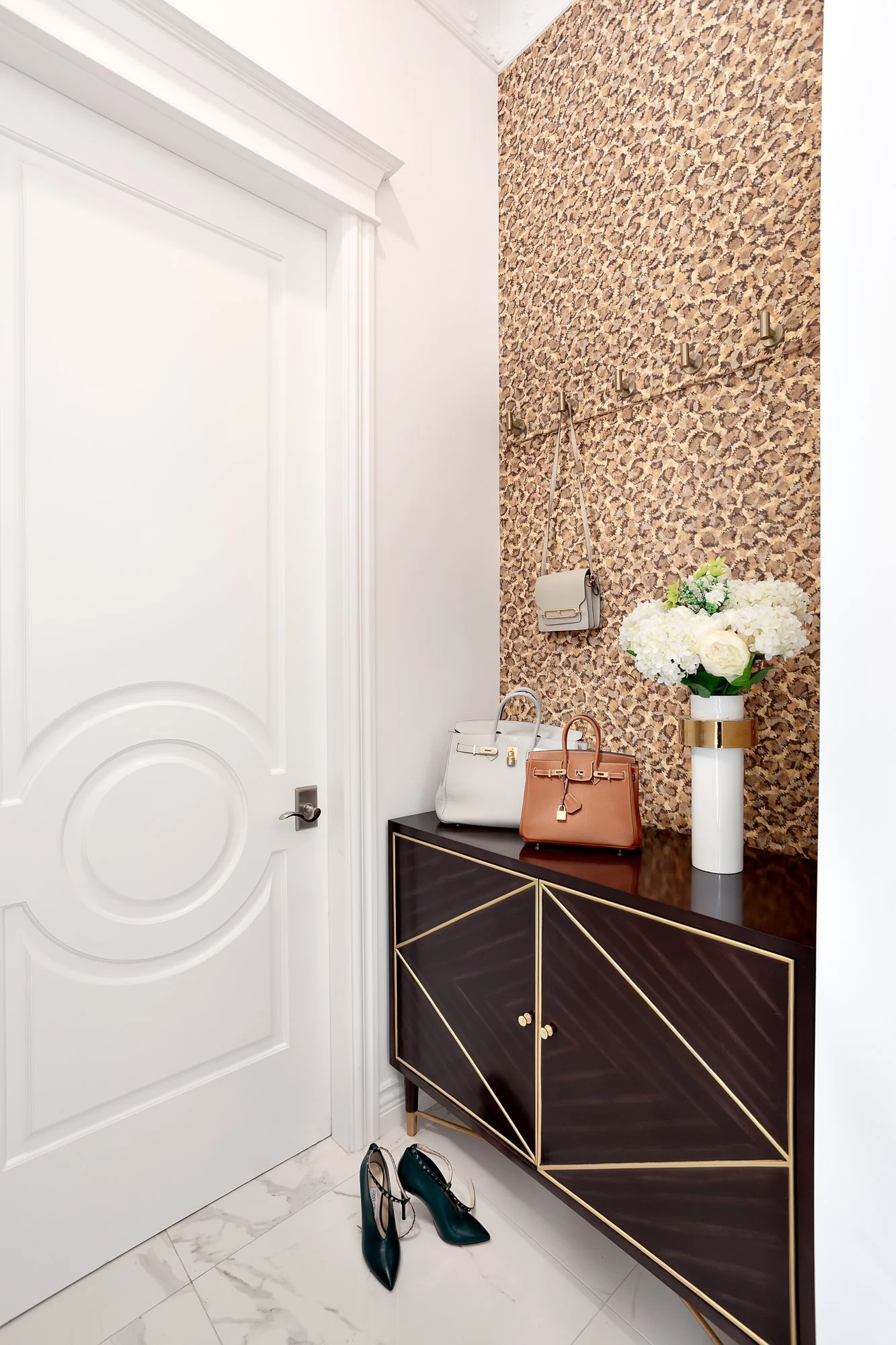 Elegant entryway detail showcasing a dark wood cabinet against a striking leopard-print wallpaper, topped with a white floral centerpiece.