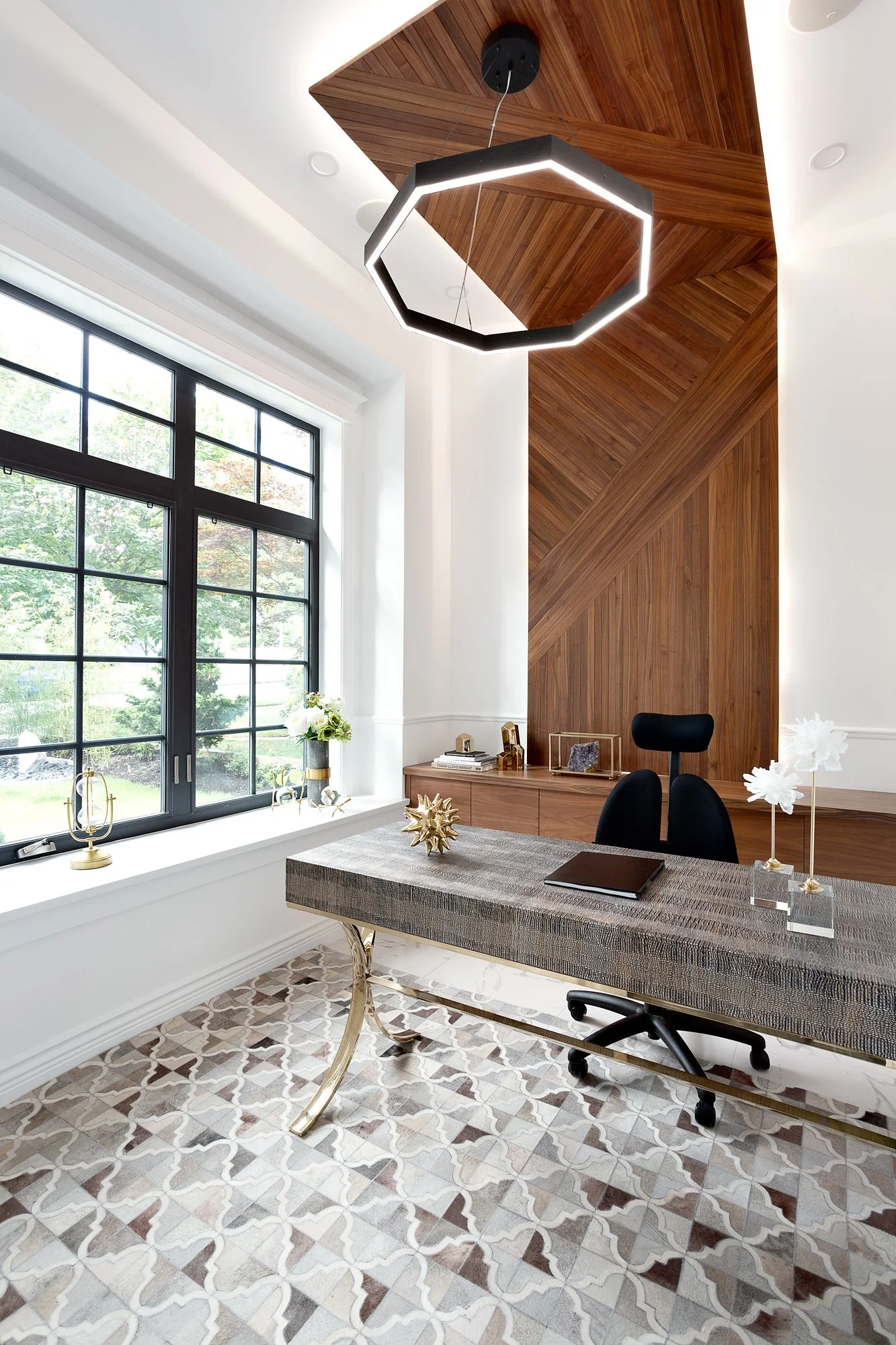 Modern home office with a dark wood herringbone feature wall, a marble-topped executive desk with gold legs, and expansive windows.