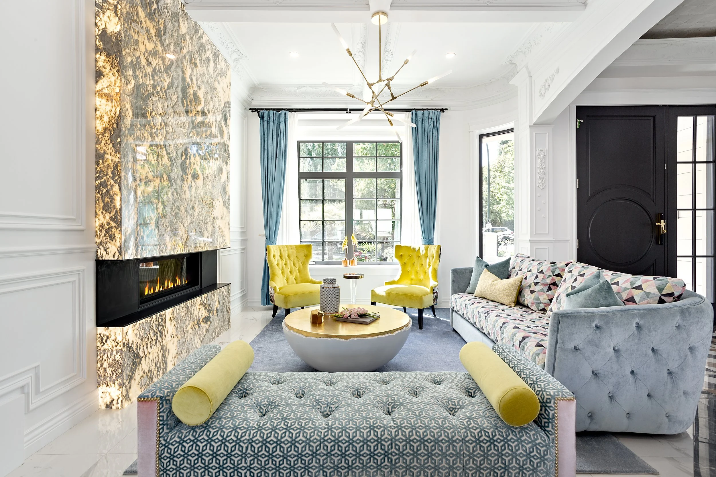 Vibrant living room with a New York townhome aesthetic, featuring a large marble fireplace, a blue patterned sofa, and yellow velvet armchairs.