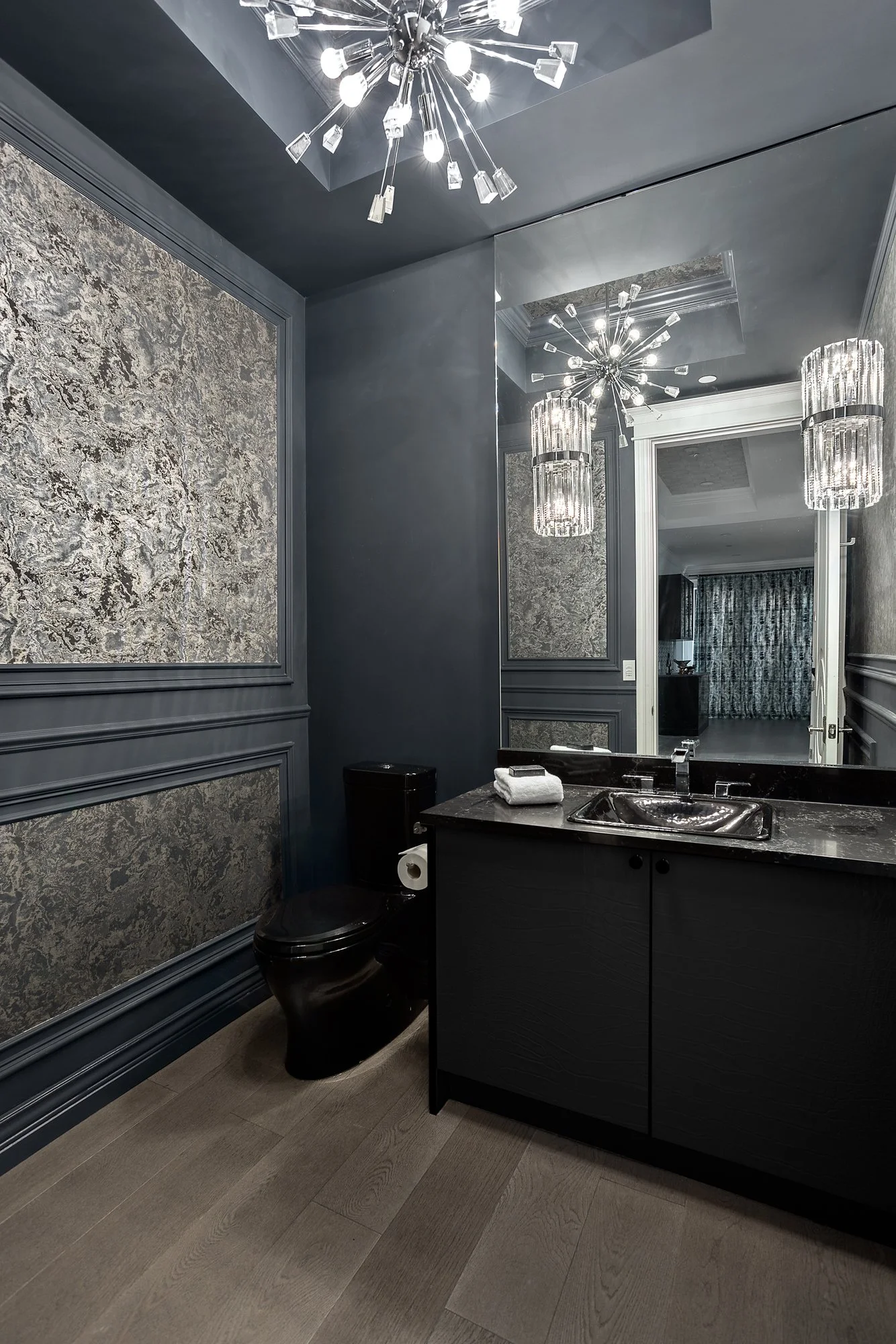 Dark and moody powder room featuring textured metallic silver wallpaper, a sleek black vanity, and modern crystal lighting.