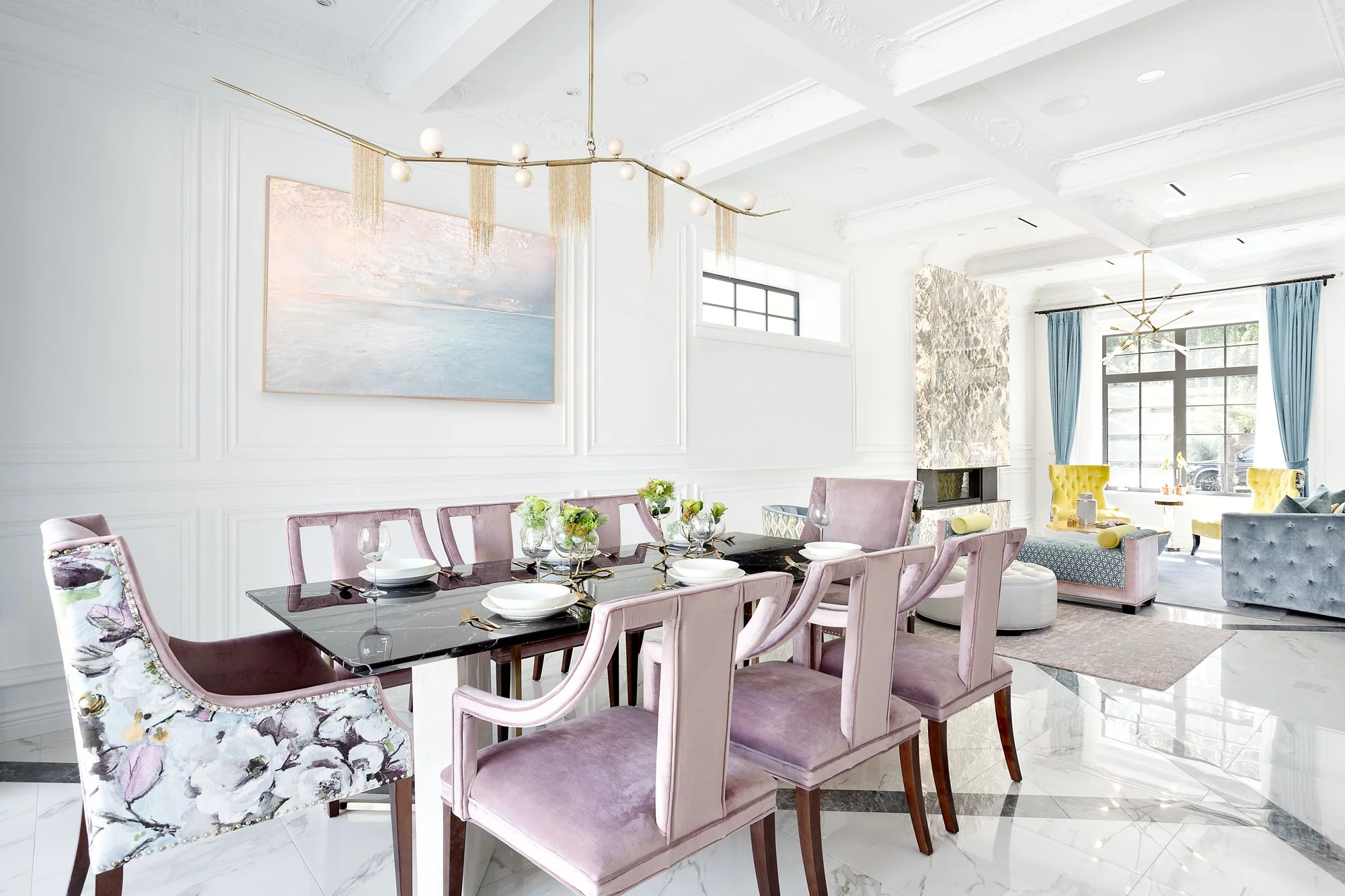 Elegant dining room featuring a glass table, lavender velvet chairs, and a sculptural gold fringe chandelier.
