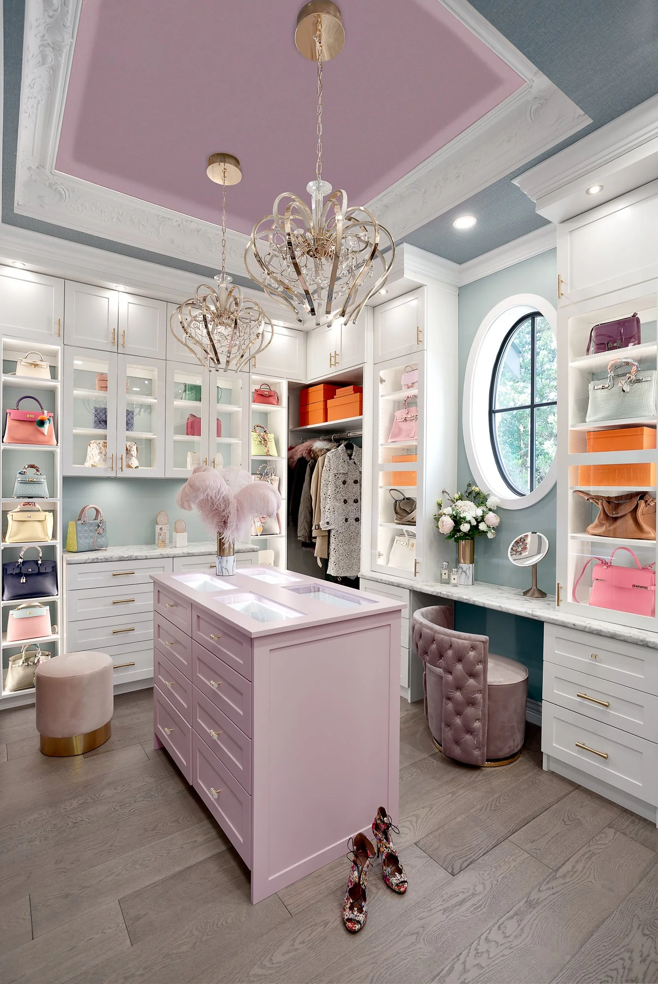 Dreamy pink walk-in closet featuring glass-front cabinetry, a central pink island, and opulent crystal chandeliers.