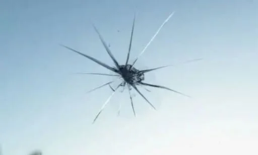 Close-up of a shattered glass window with a crack radiating outwards.